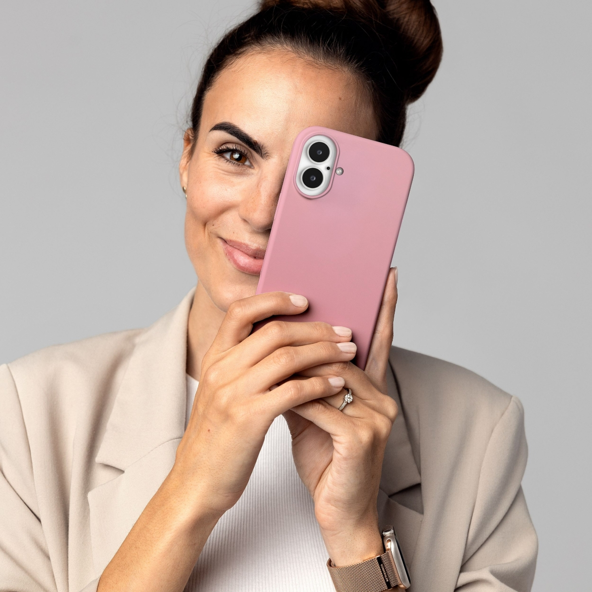 Donna sorridente, tiene una custodia rosa per telefono, anello al dito, indossa un blazer beige, acconciatura a chignon.