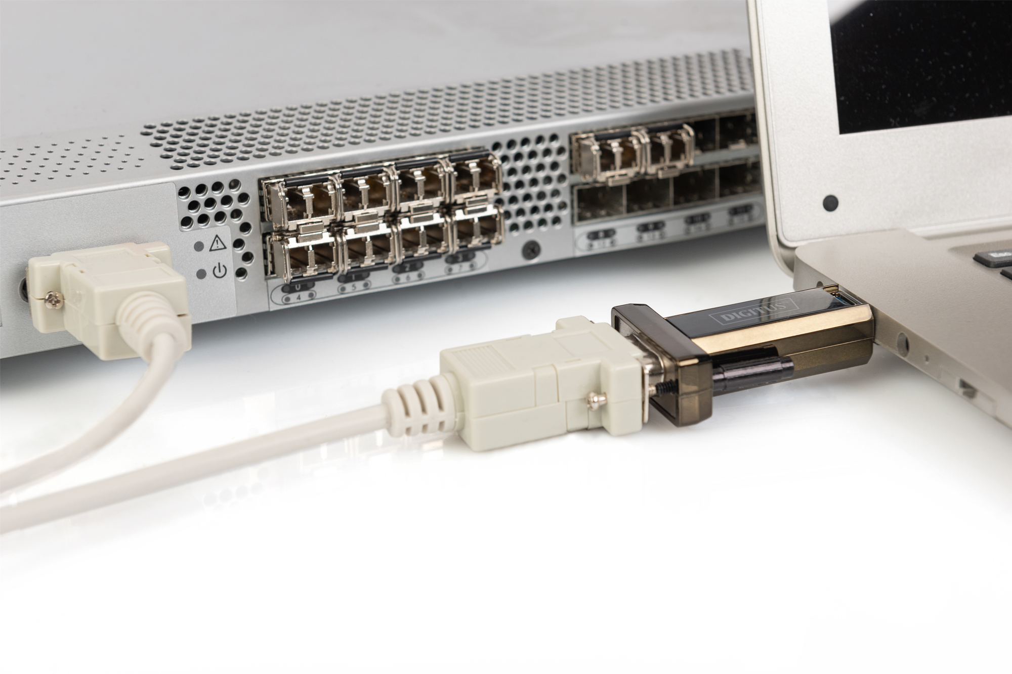Un server argentato collegato a un laptop tramite un adattatore USB-seriale nero.