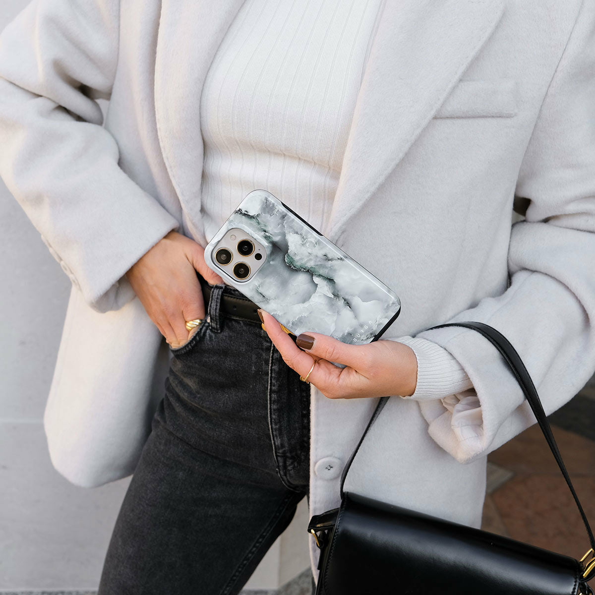 Donna che tiene un telefono in una custodia di marmo. Il telefono è tenuto davanti a uno sfondo grigio.
