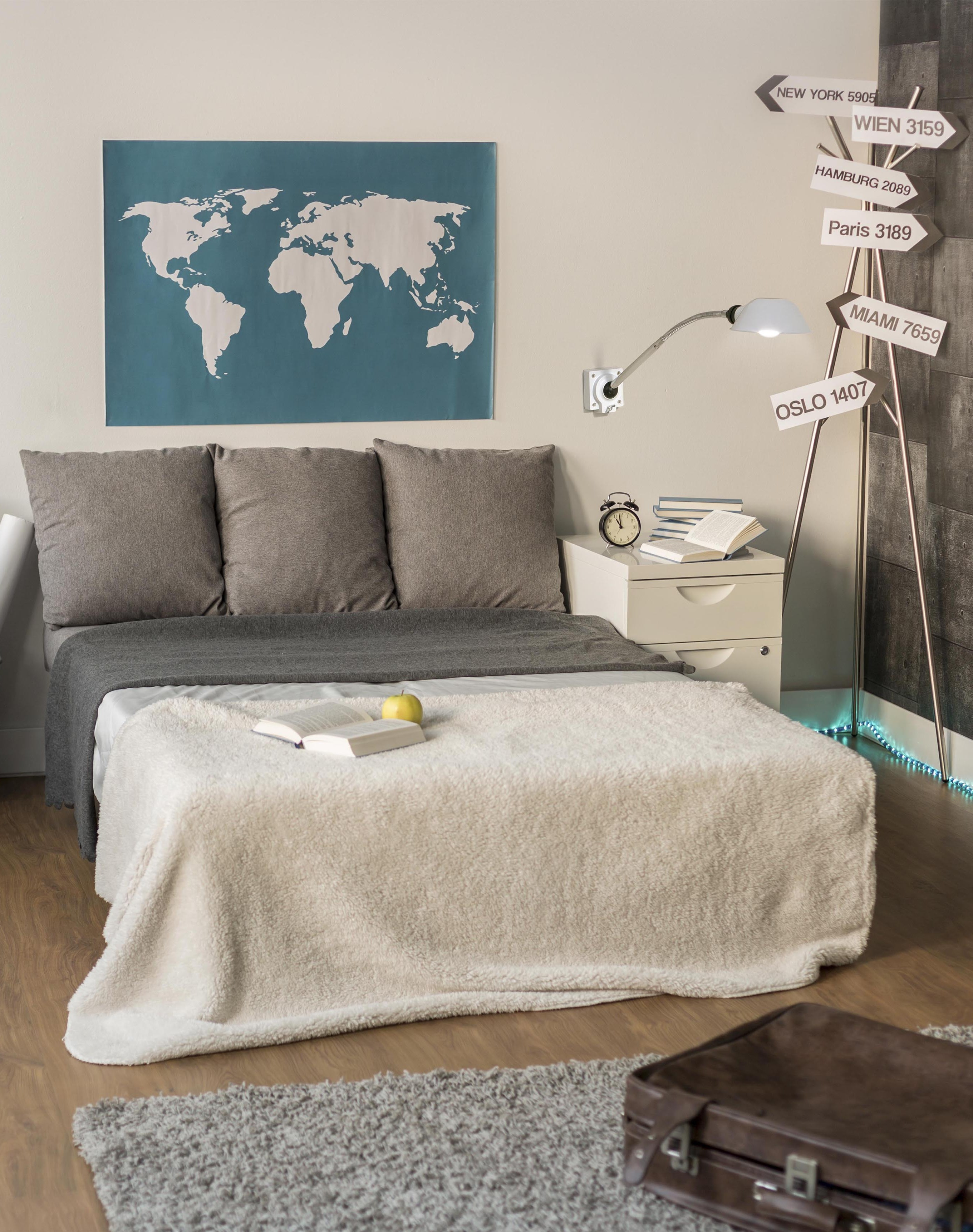 Slaapkamer met bed, kaart, nachtkastje en wereldkaart. Een leeslamp aan de muur.