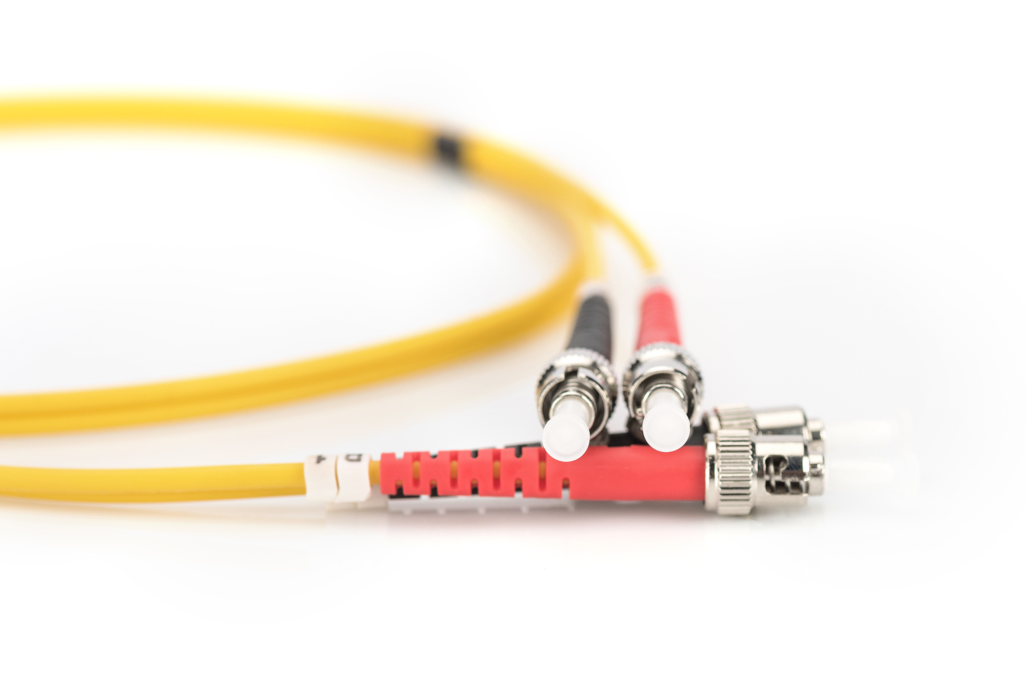 Cavo in fibra ottica giallo con connettori rossi e neri, sfondo bianco. Focus sui connettori.