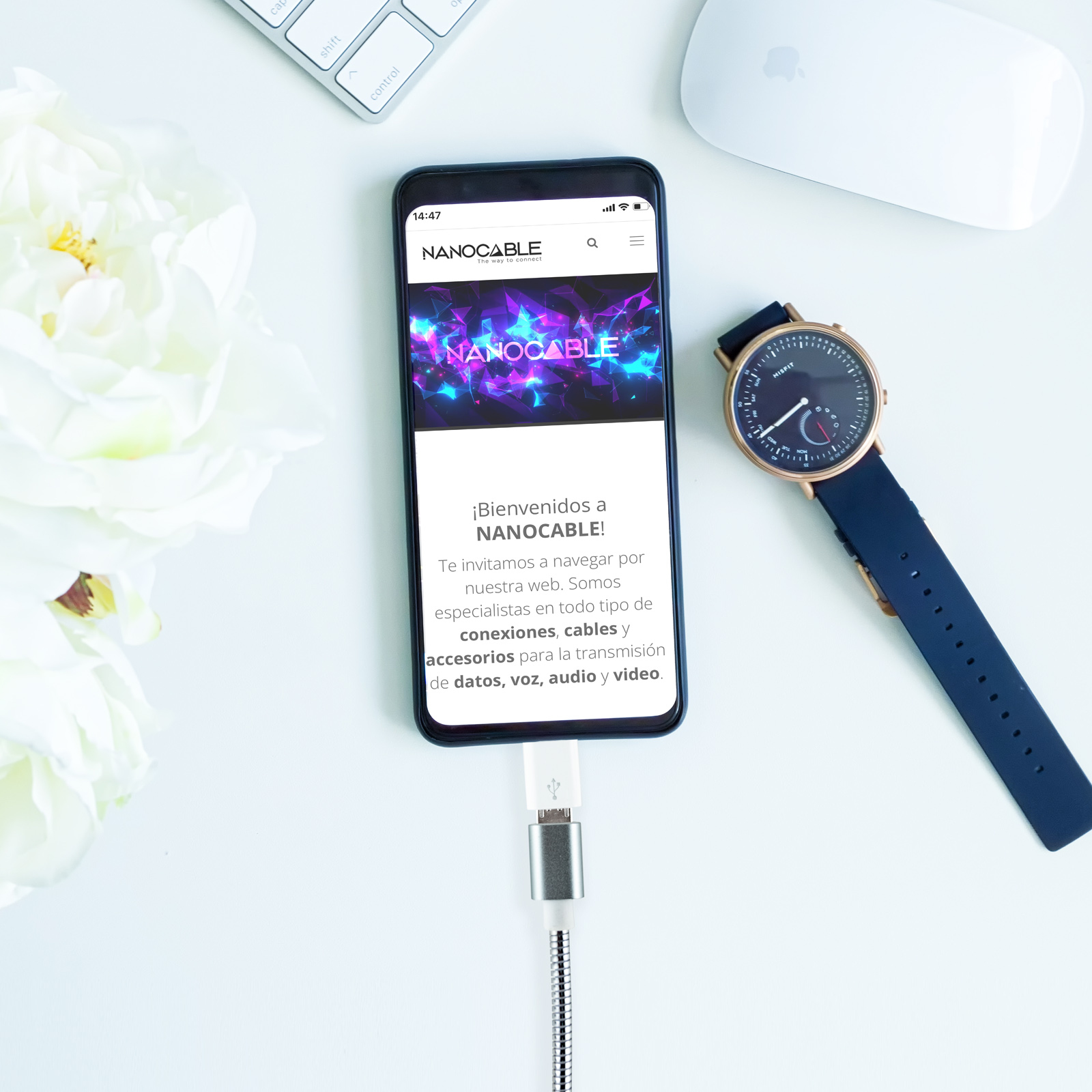 Smartphone con cavo di ricarica, orologio, fiori, tastiera, mouse, sfondo bianco.