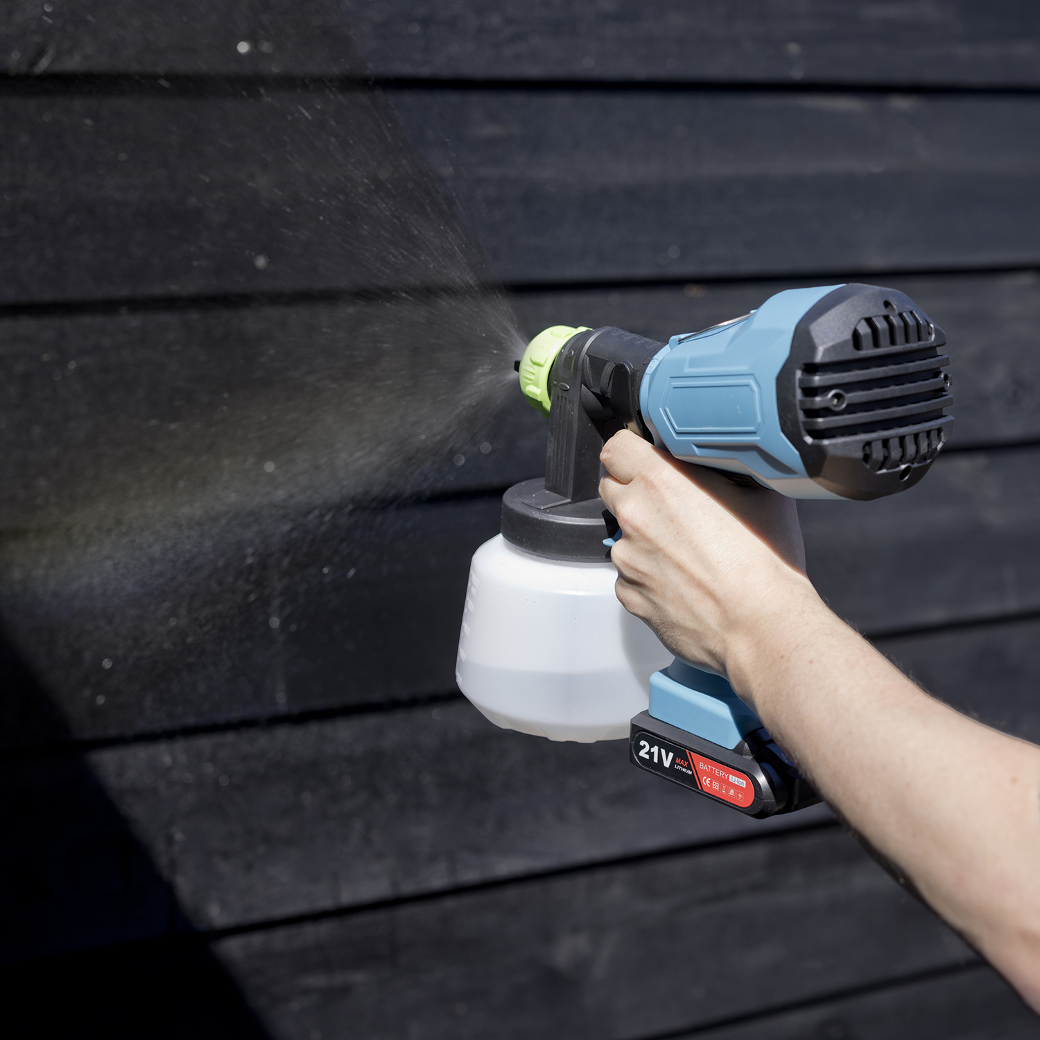 Een persoon spuit een zwarte houten schutting met een blauw-zwarte verfspuit.