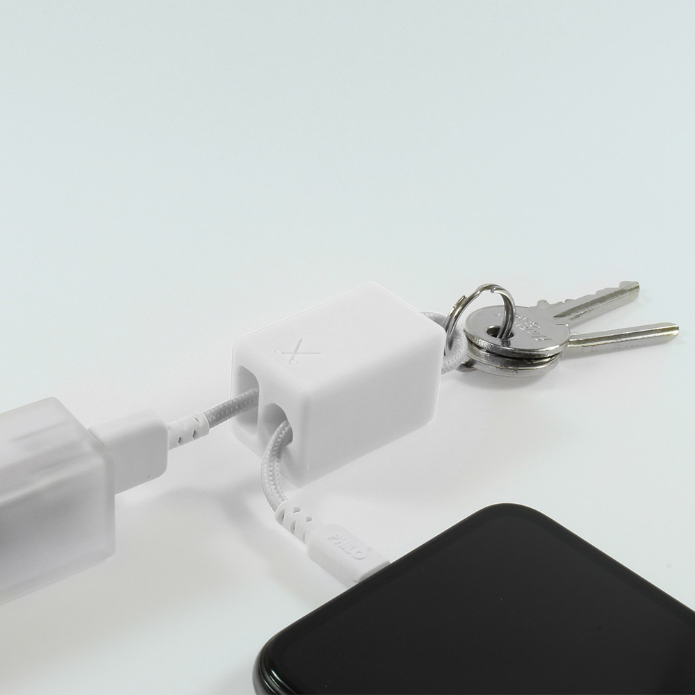 Un adattatore bianco che collega due cavi, con un portachiavi e un telefono. Sfondo bianco.