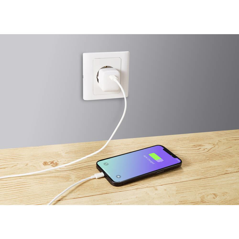 Uno smartphone in carica, collegato a una presa a muro su un tavolo di legno contro un muro grigio.
