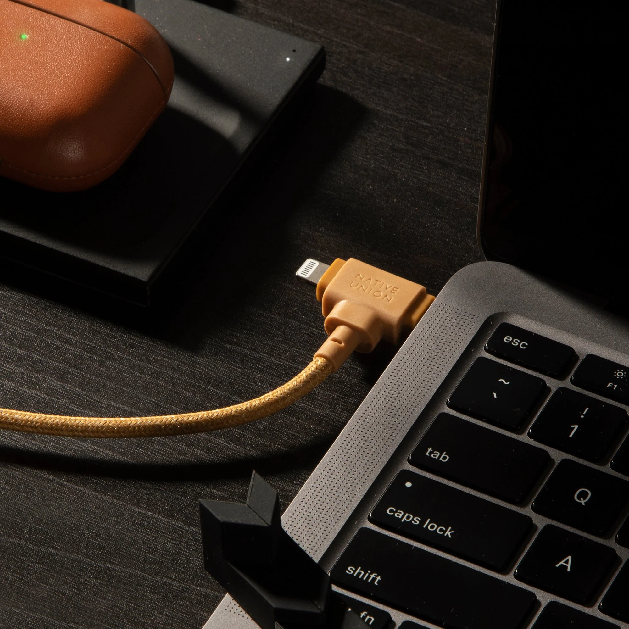 Un laptop in carica con un cavo Native Union, vicino a una custodia e un taccuino.