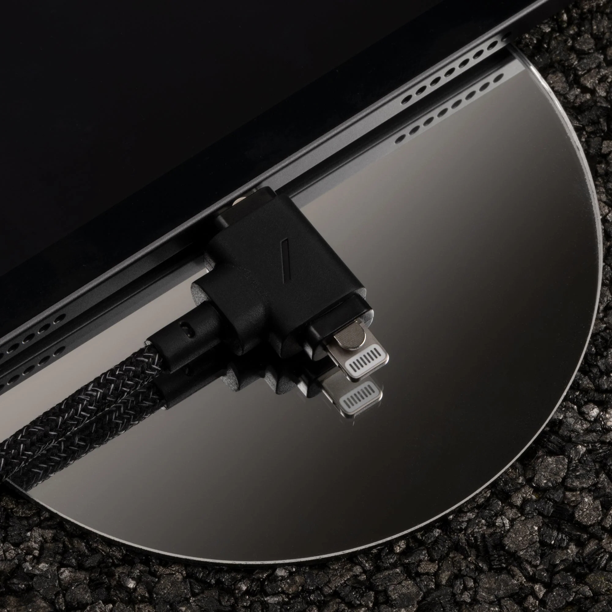 Cavo di ricarica nero su superficie riflettente, con connettore lightning visibile.