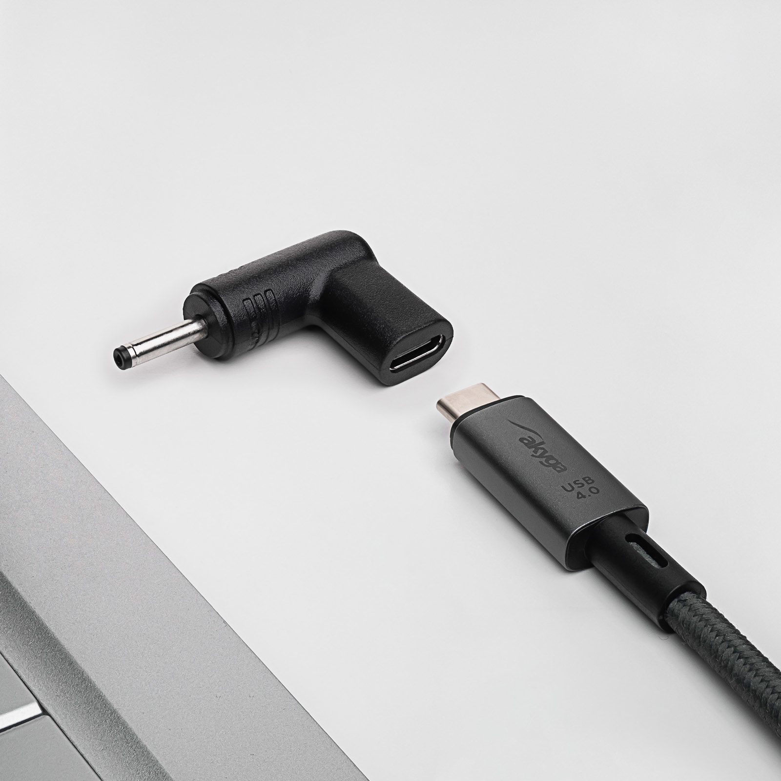 Adattatore nero a L con jack DC e cavo USB-C, su una superficie grigio chiaro.