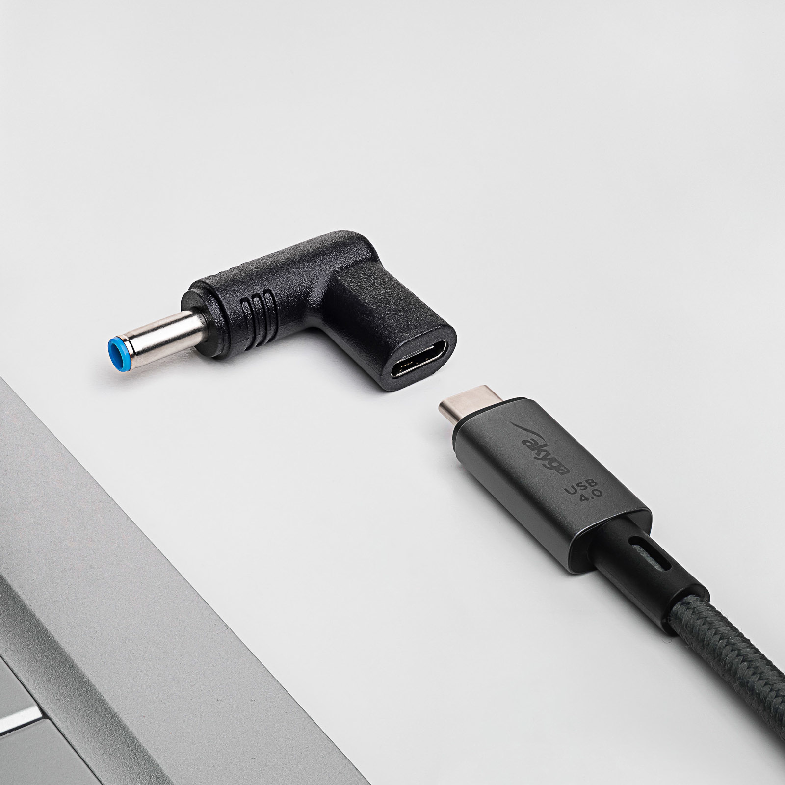 Cavo USB-C nero e grigio accanto a un adattatore angolato nero. Superficie bianca.