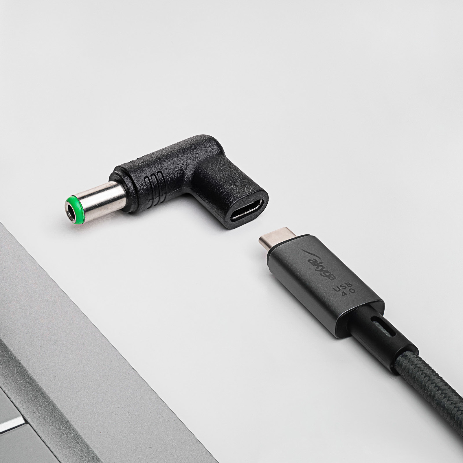 Cavo USB-C nero e grigio accanto a un adattatore angolato nero. Superficie bianca.