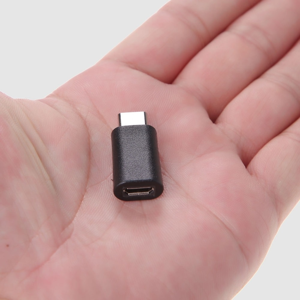 Un adattatore USB-C nero tenuto in una mano su sfondo bianco.