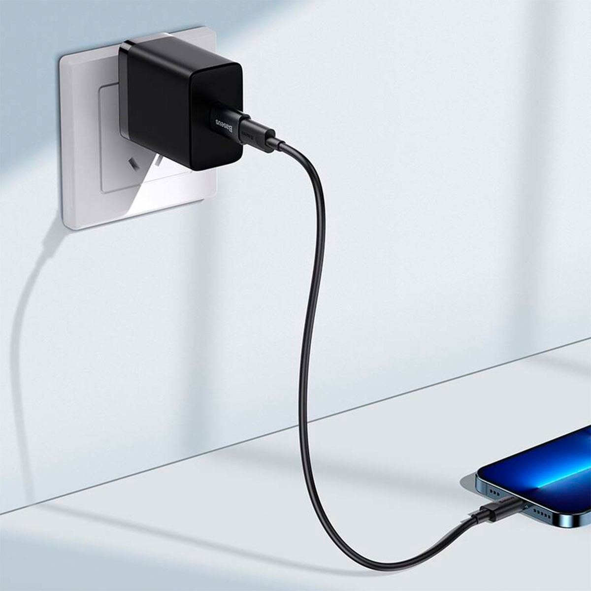 Czarna ładowarka podłączona do gniazdka ściennego, ładująca telefon.