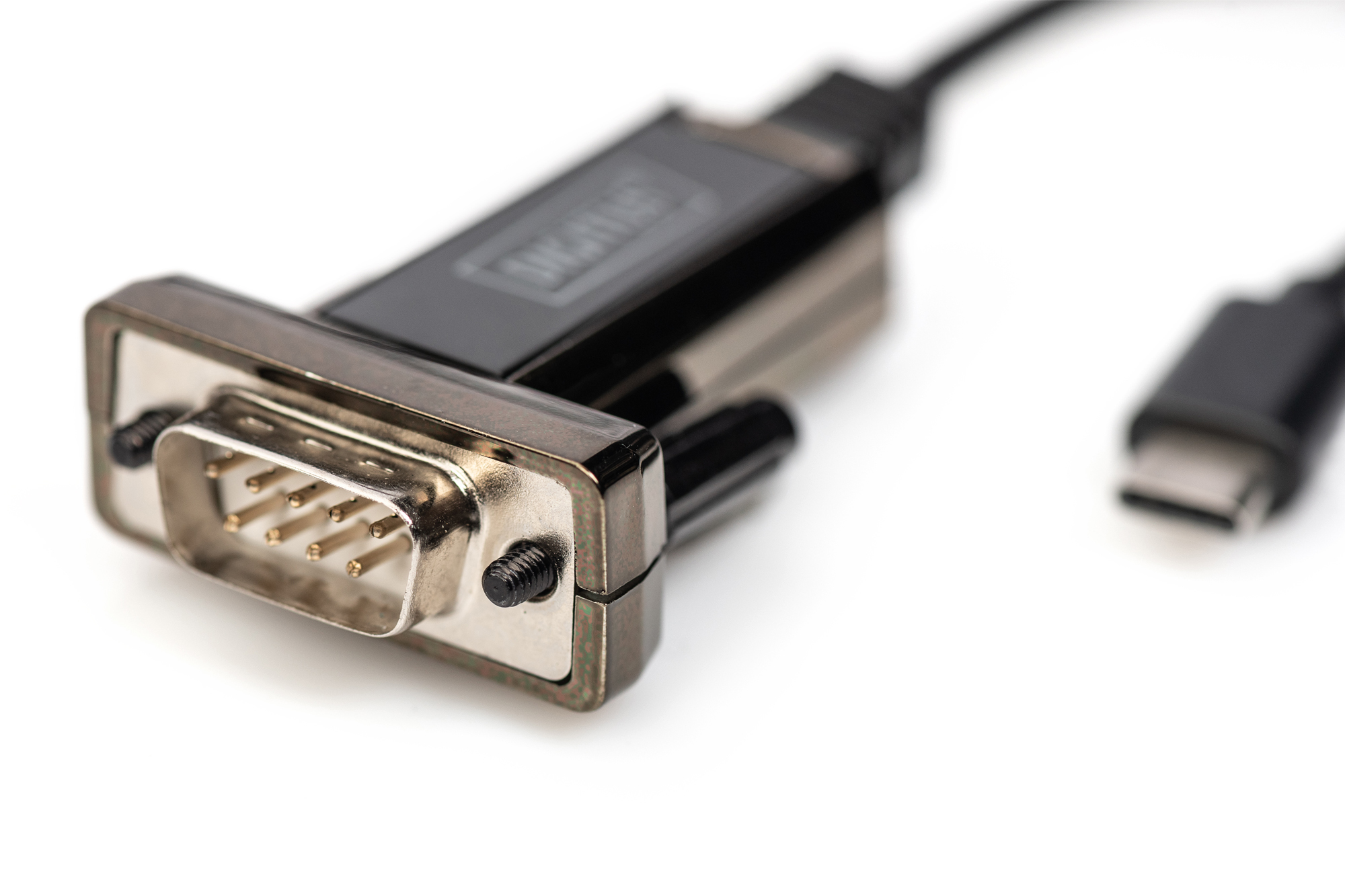 Zbliżenie adaptera USB-C na szeregowy. Adapter jest czarny ze srebrnym złączem.