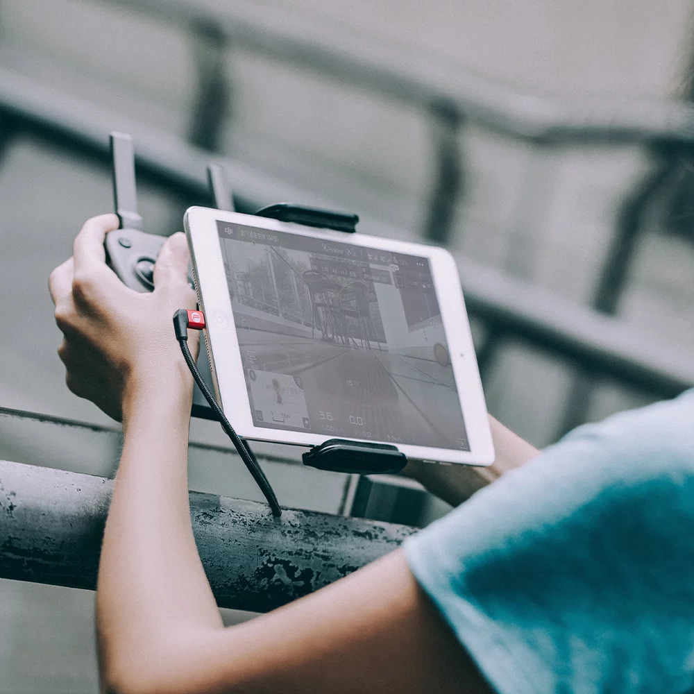 Osoba trzymająca tablet podłączony do pilota drona kablem.