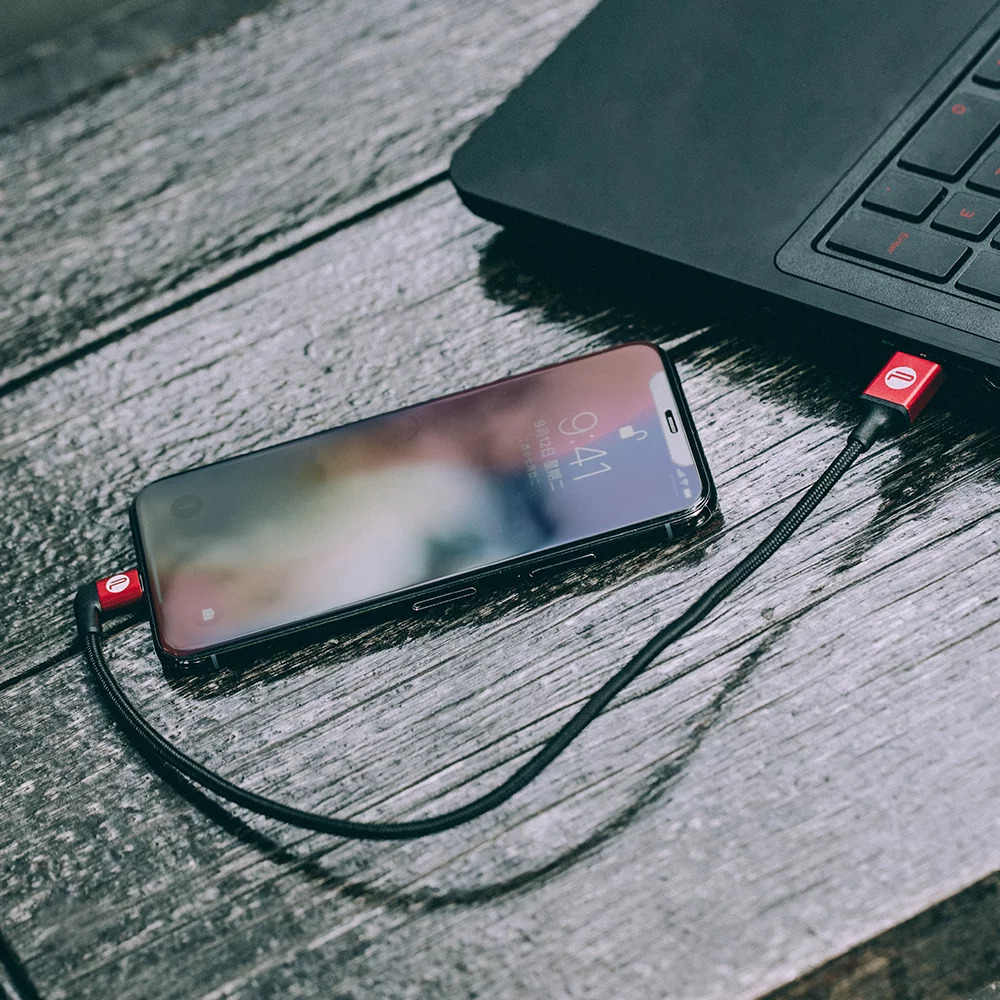 Smartfon z kablem ładującym podłączony do laptopa na drewnianym stole.