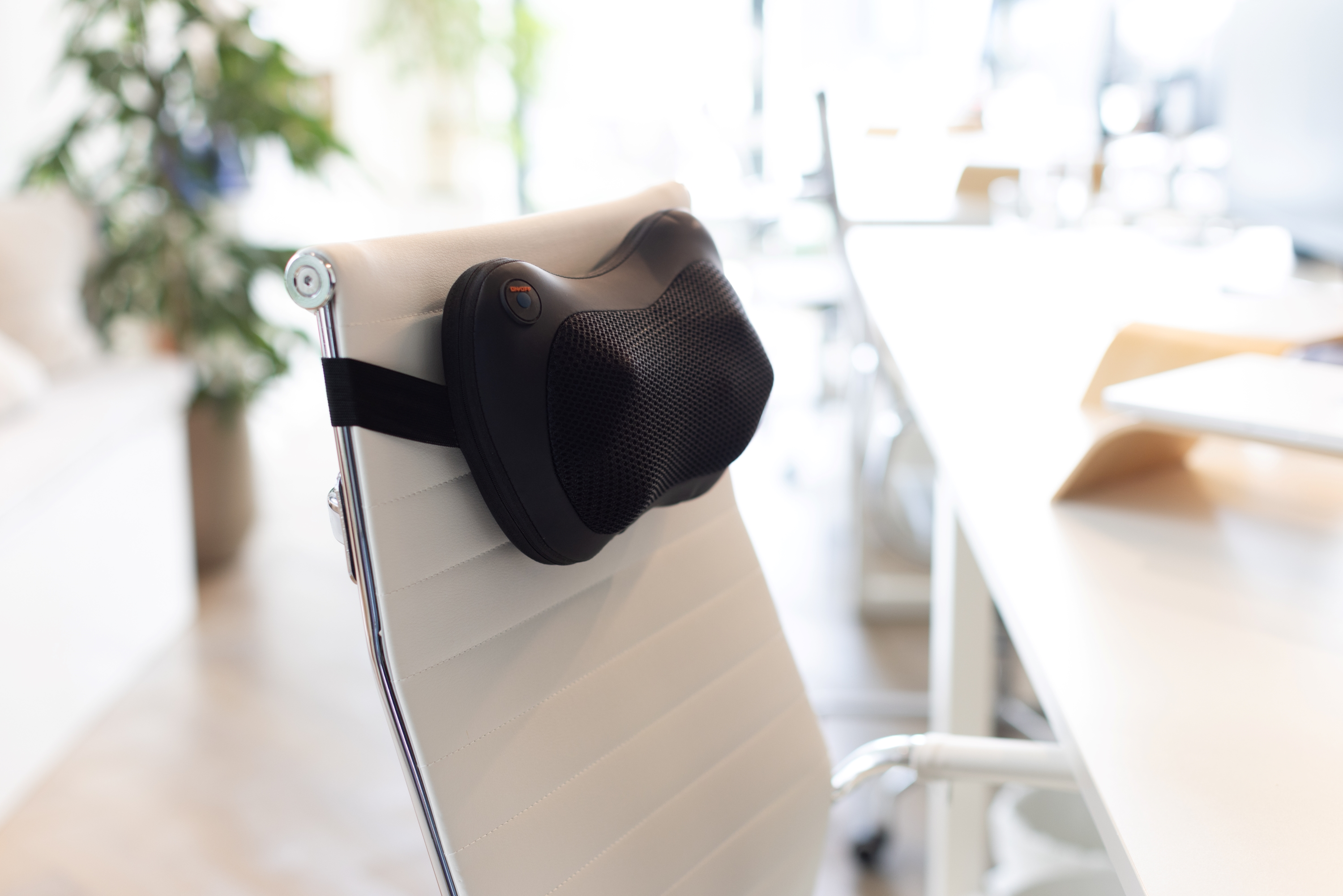 Black neck massager on a white office chair. Background is an office setting.