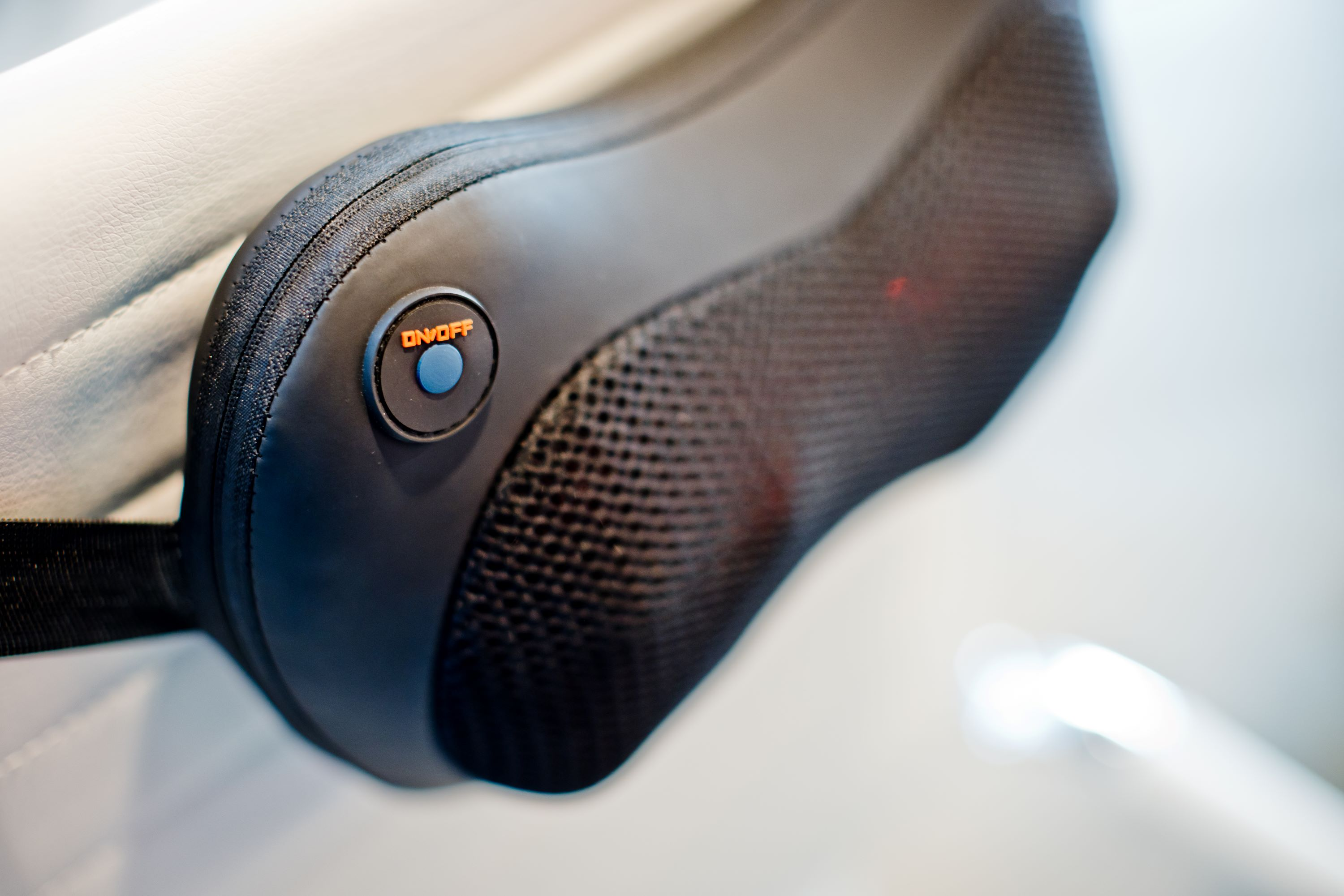 A black massage device with an on/off button and mesh surface on a white surface.