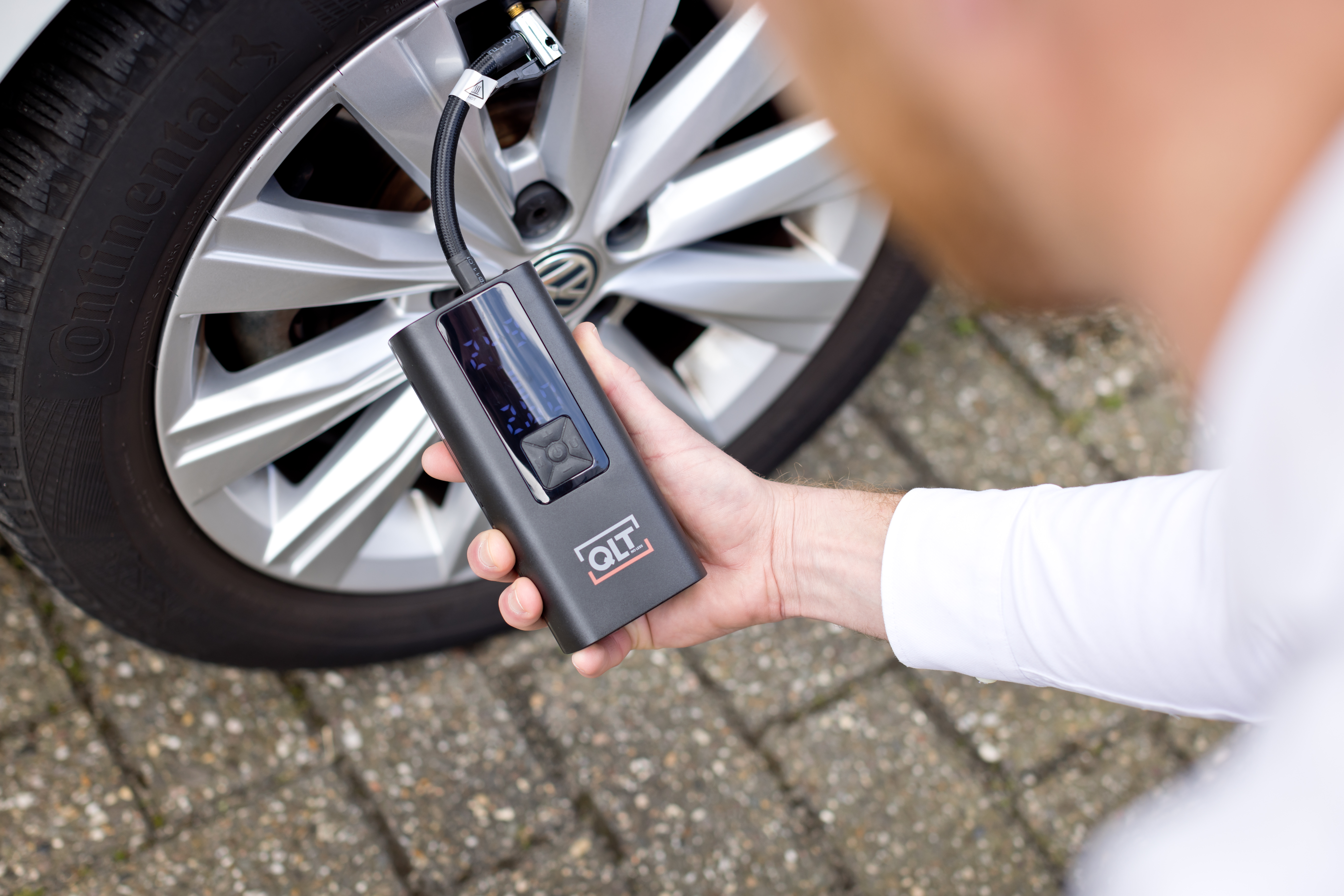 A person is holding a black QLT tire inflator next to a car tire.