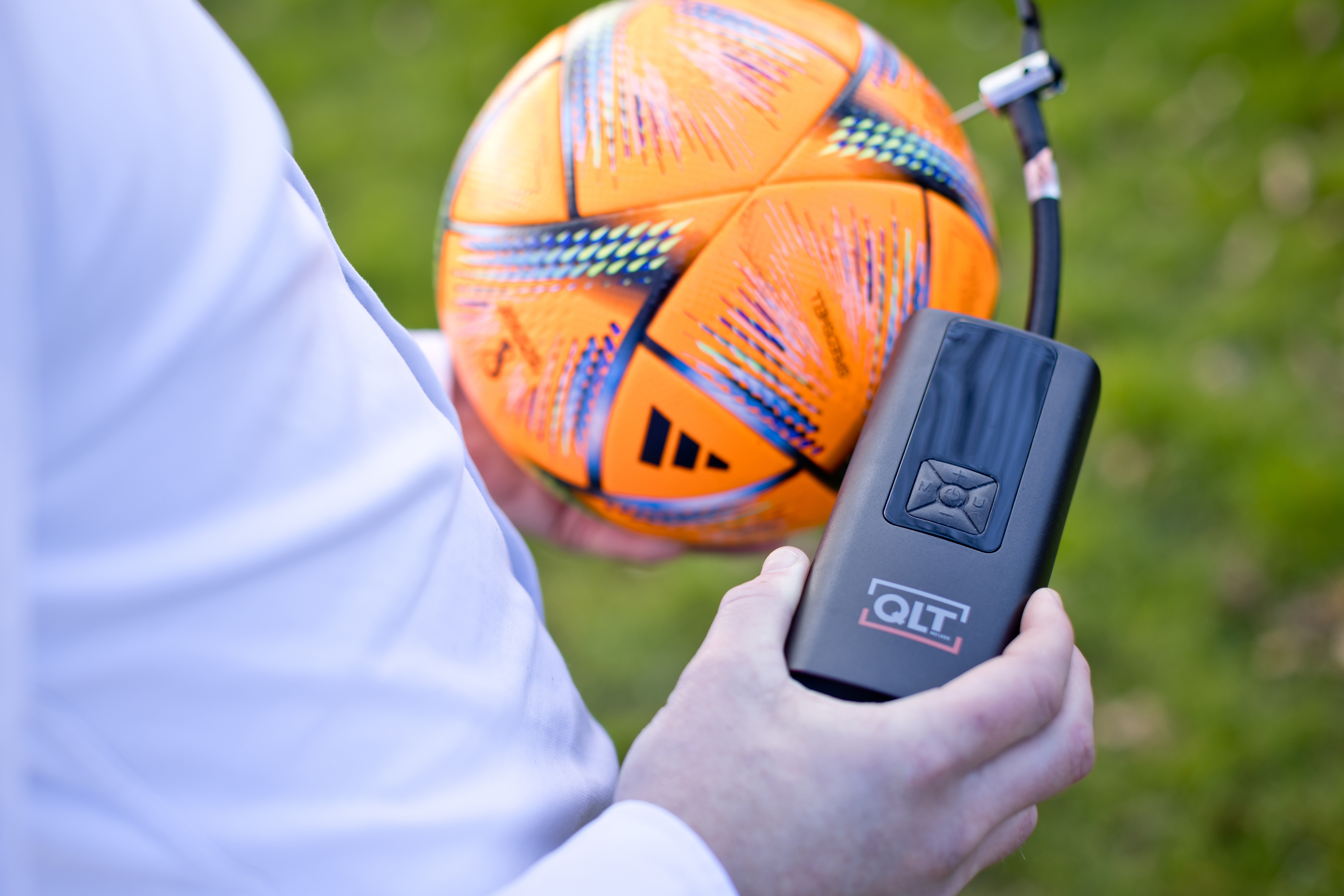 A person inflates an orange soccer ball with an air pump. The ball has black designs.