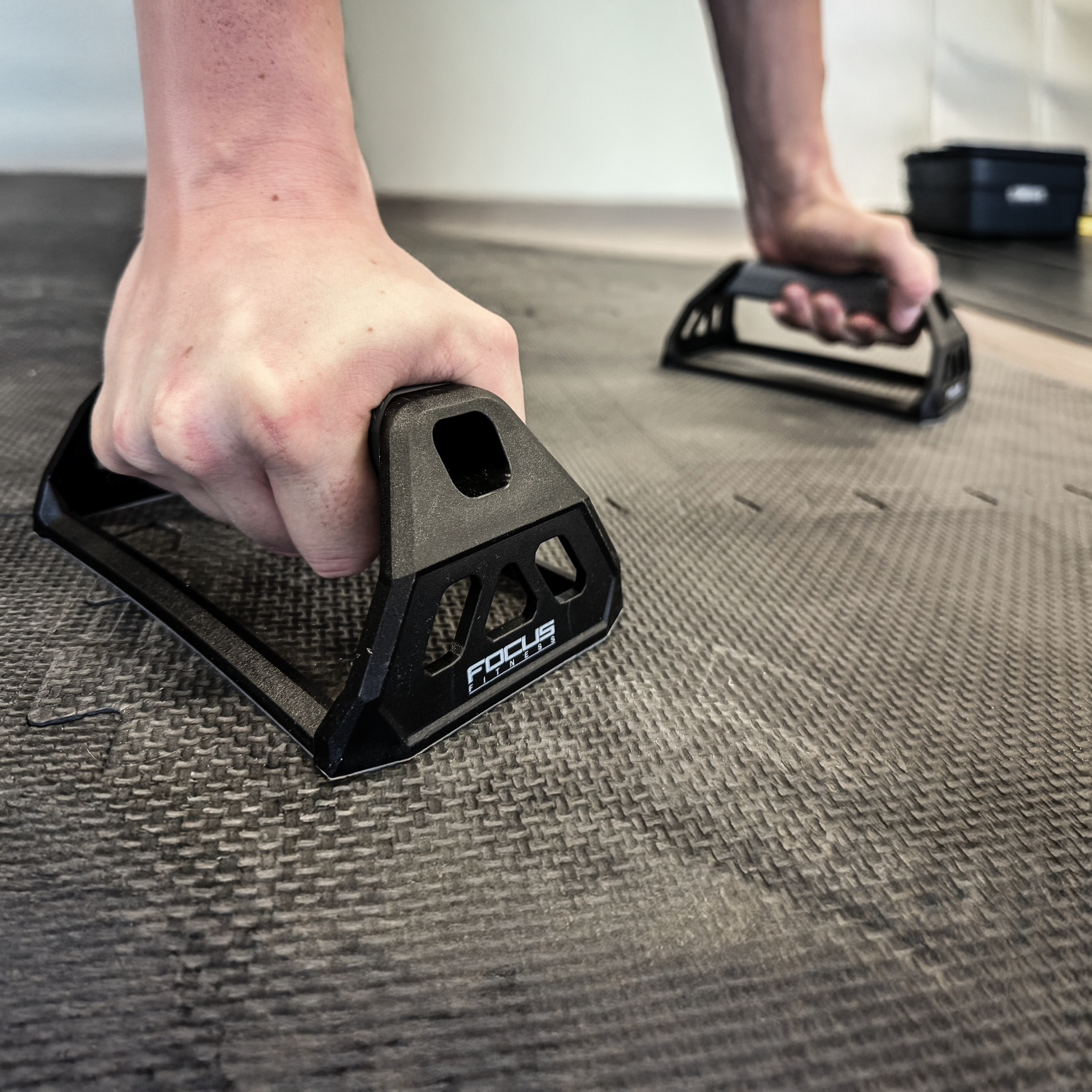 Person doing push-ups on a mat using black push-up bars. Hands are gripping the bars.
