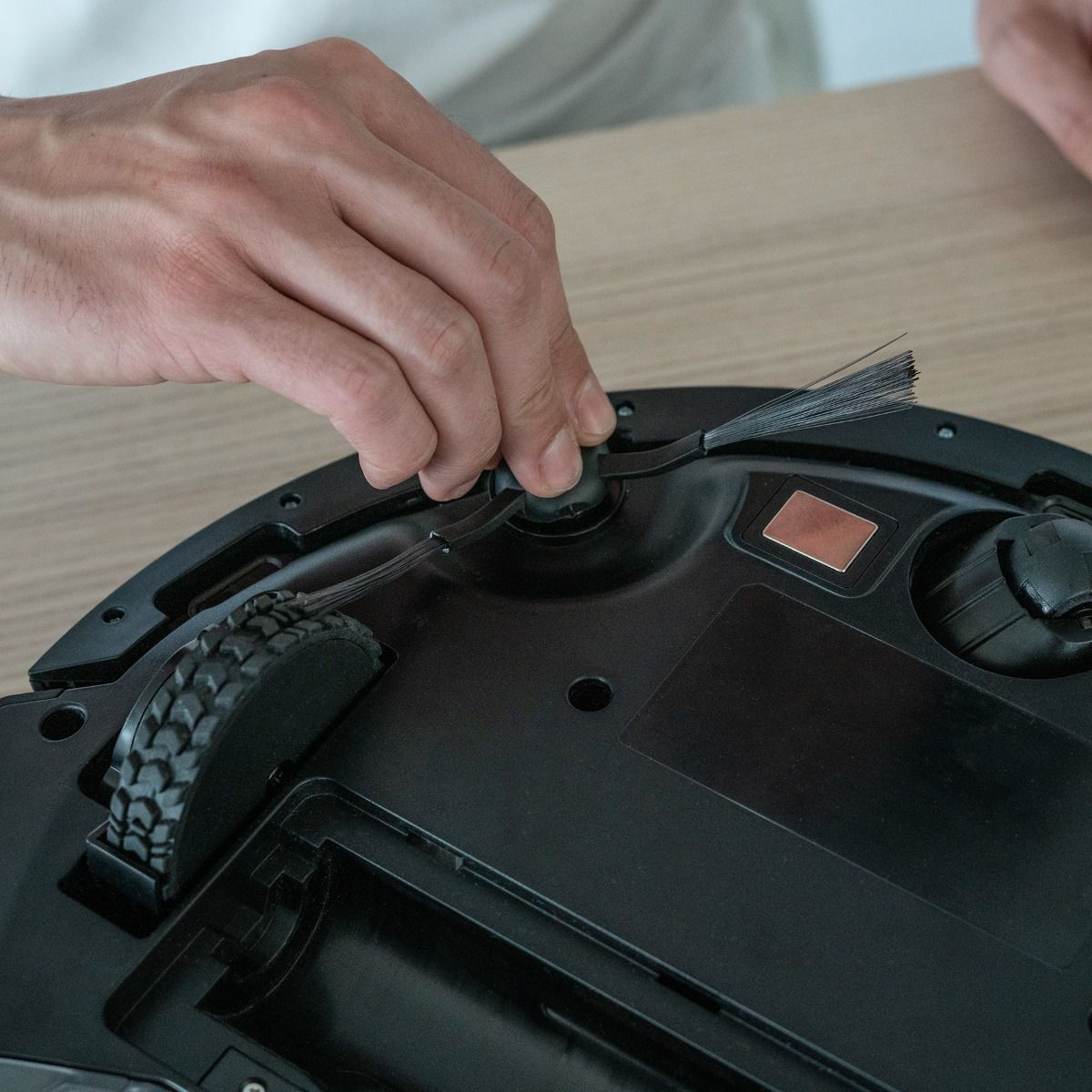 Ręka osoby czyszczącej odkurzacz automatyczny. Odkurzacz jest czarny i okrągły.