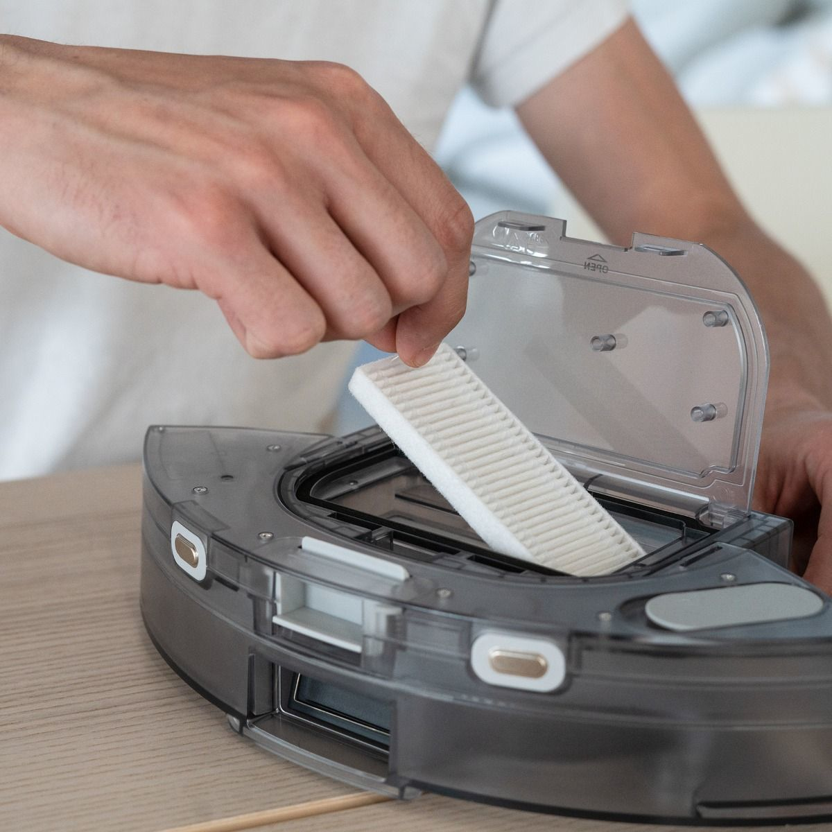 Osoba wkłada filtr do robota sprzątającego. Szary robot z białym filtrem.