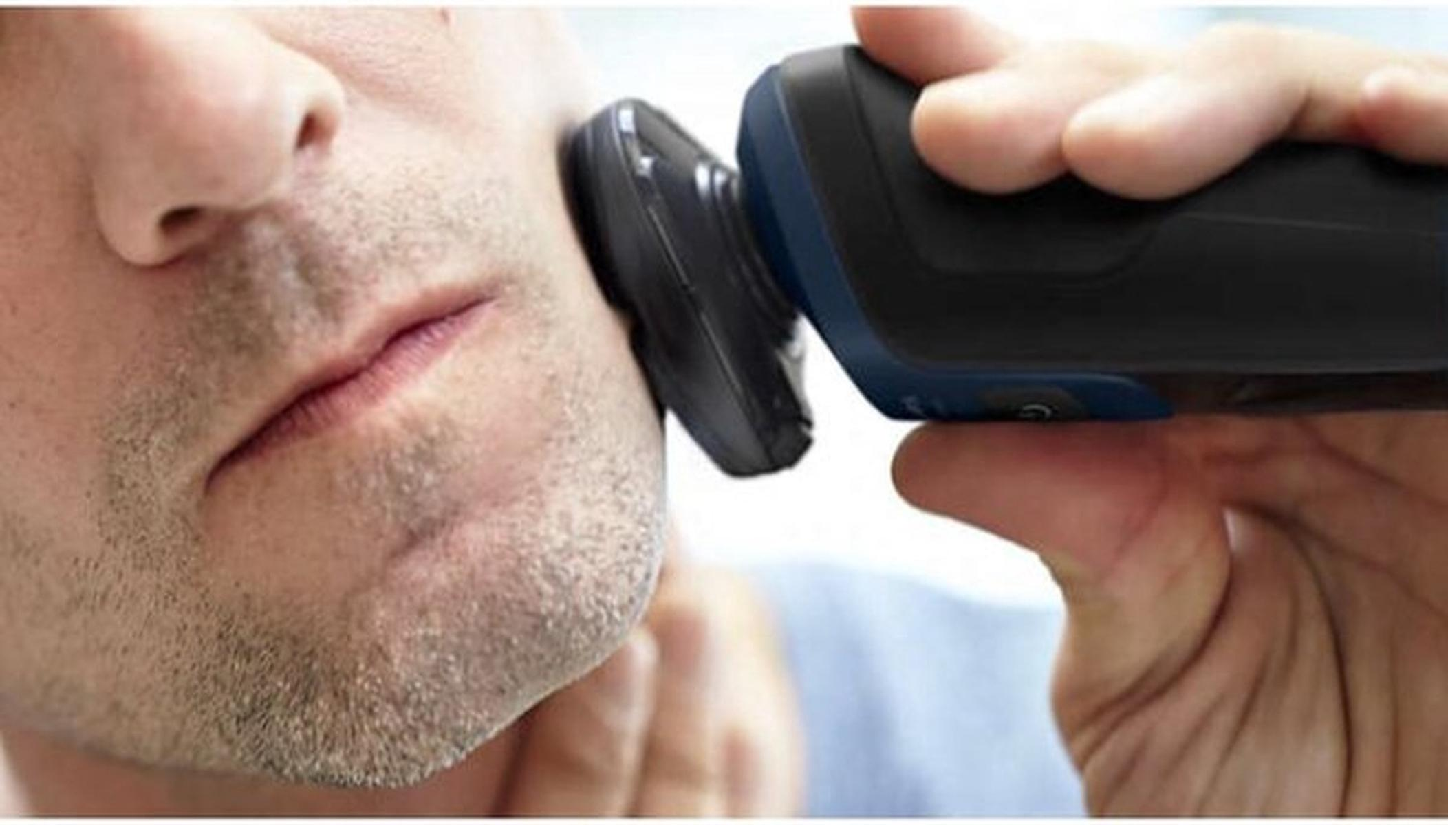Close-up of a man shaving his cheek with a black electric shaver.
