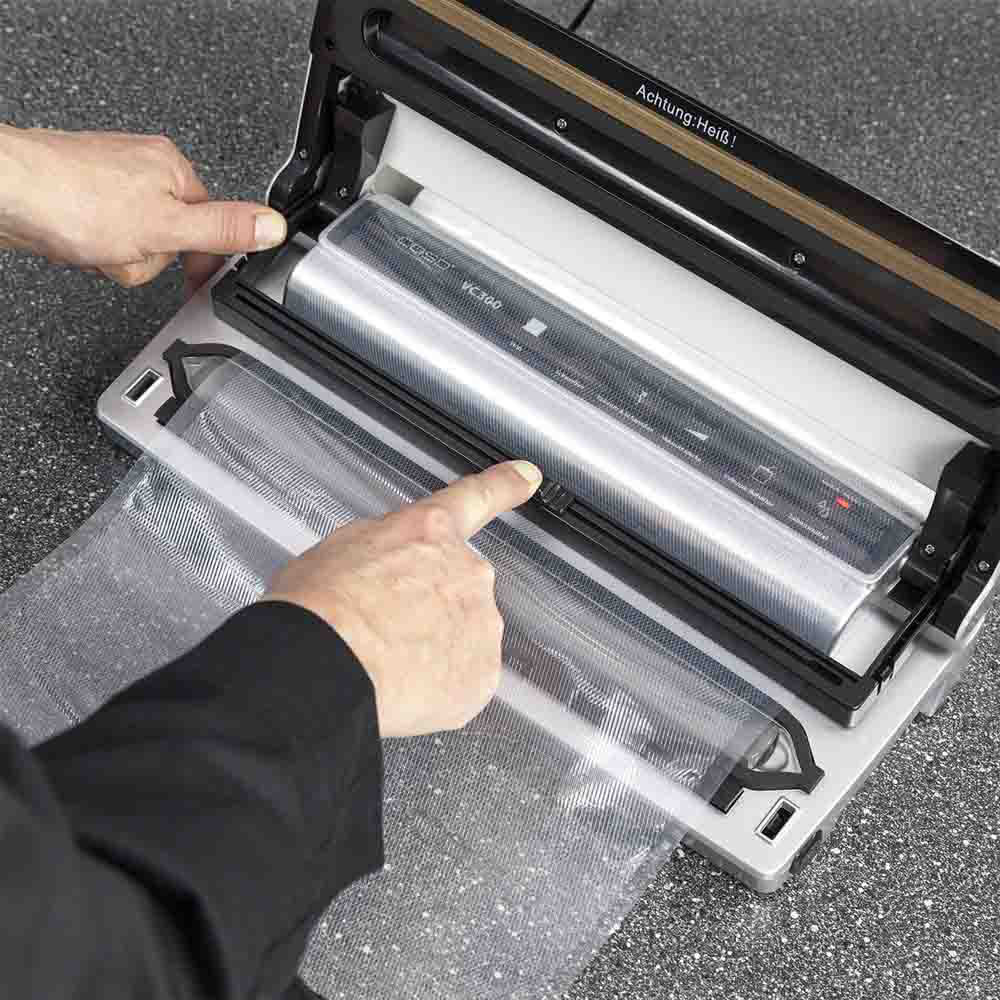 Mani di una persona che utilizza una termosigillatrice sottovuoto. La macchina è argento e nera, con superficie grigia.