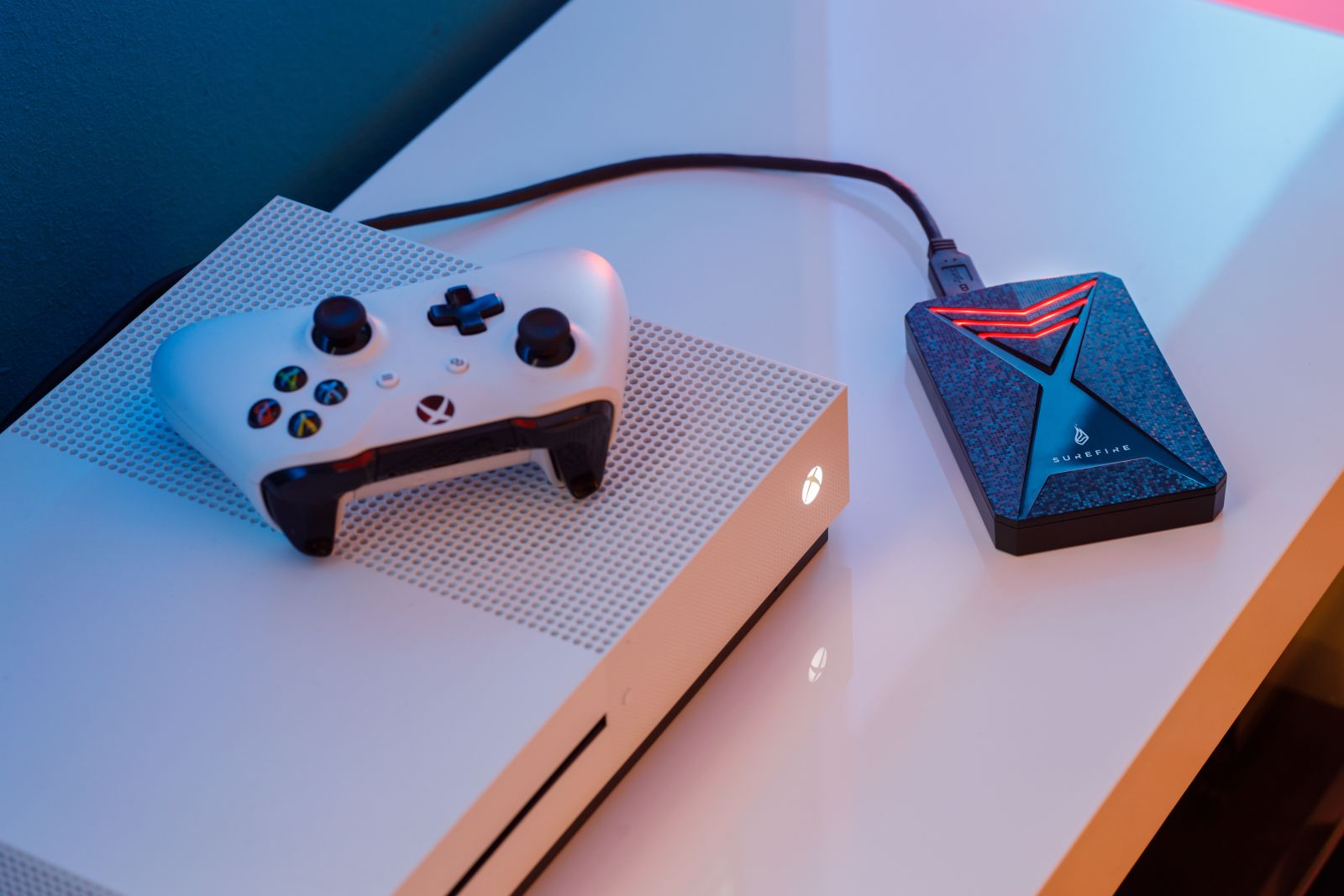 Konsola Xbox One z białym kontrolerem i czarnym dyskiem twardym zewnętrznym Supersonic. Biała powierzchnia.