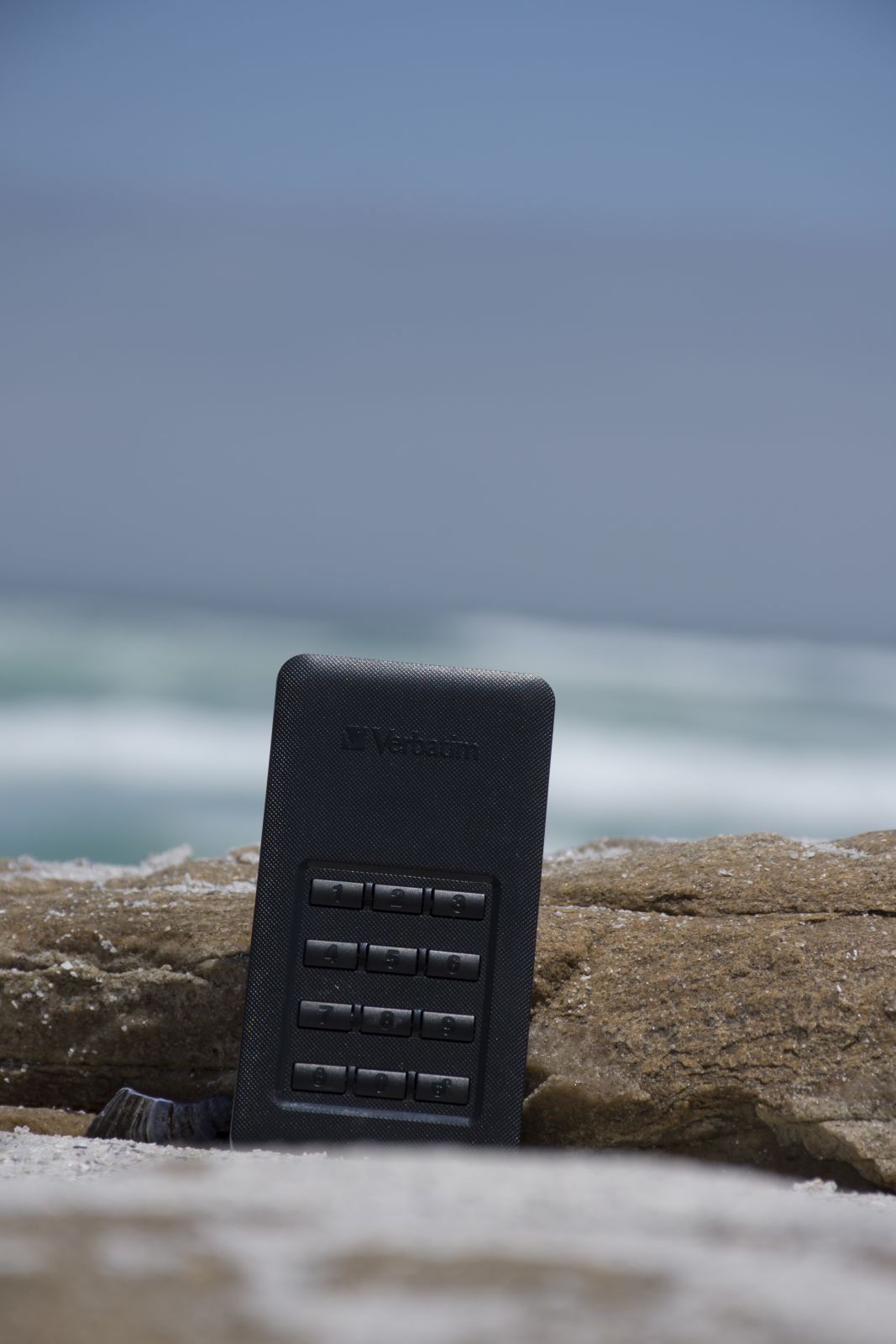 Czarne, prostokątne urządzenie Verbatim na skale. Tło oceanu.
