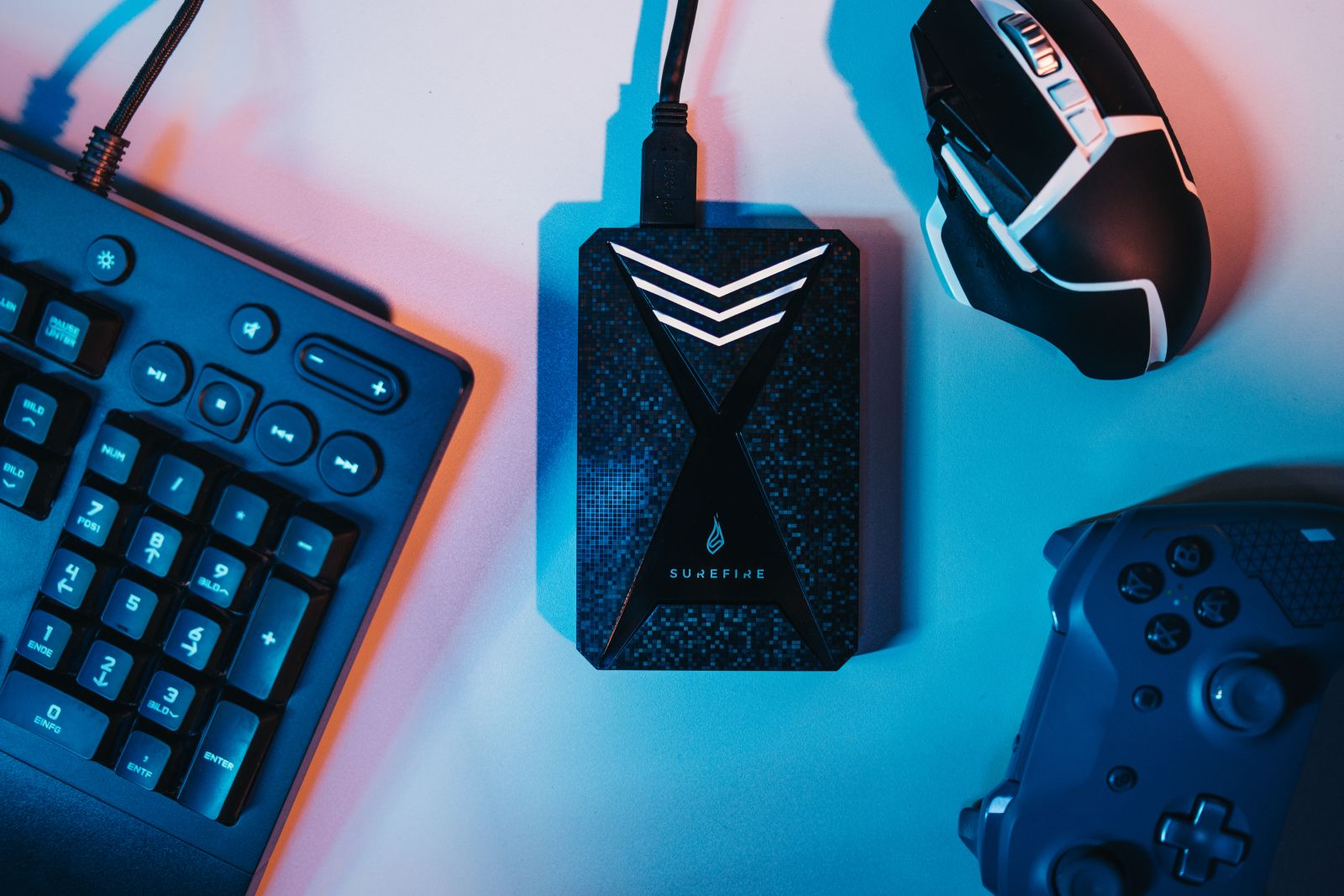 Zestaw technologiczny z klawiaturą, myszą, dyskiem zewnętrznym i kontrolerem na niebieskiej powierzchni.