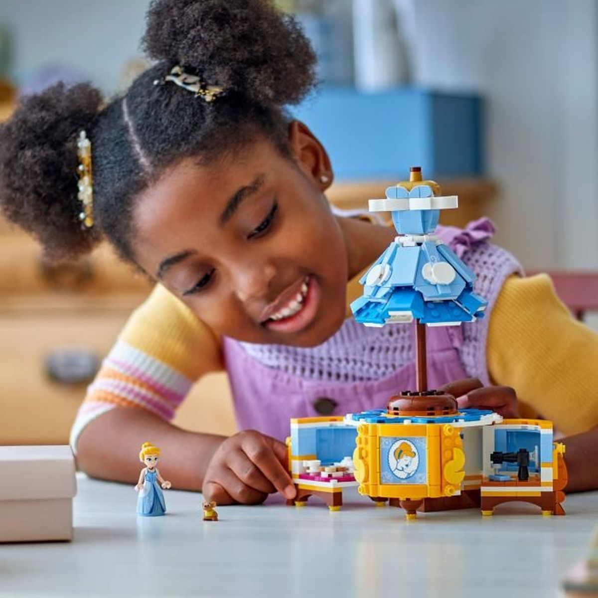 Dziewczynka bawi się zestawem Lego. Niebieska sukienka i zabawka przed nią.