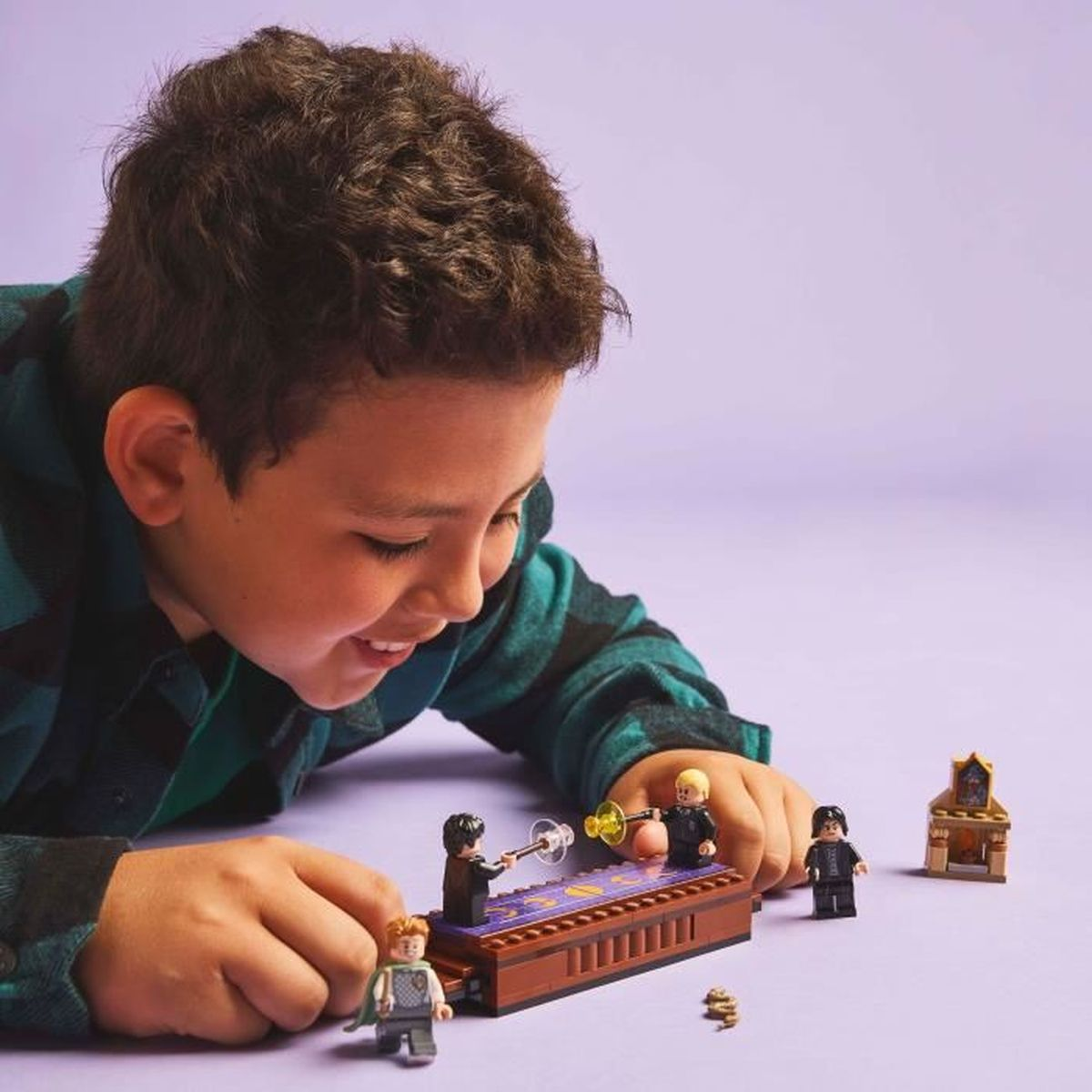 Chłopiec bawiący się zestawem Lego Harry Potter. Uśmiechnięty. Fioletowe tło.