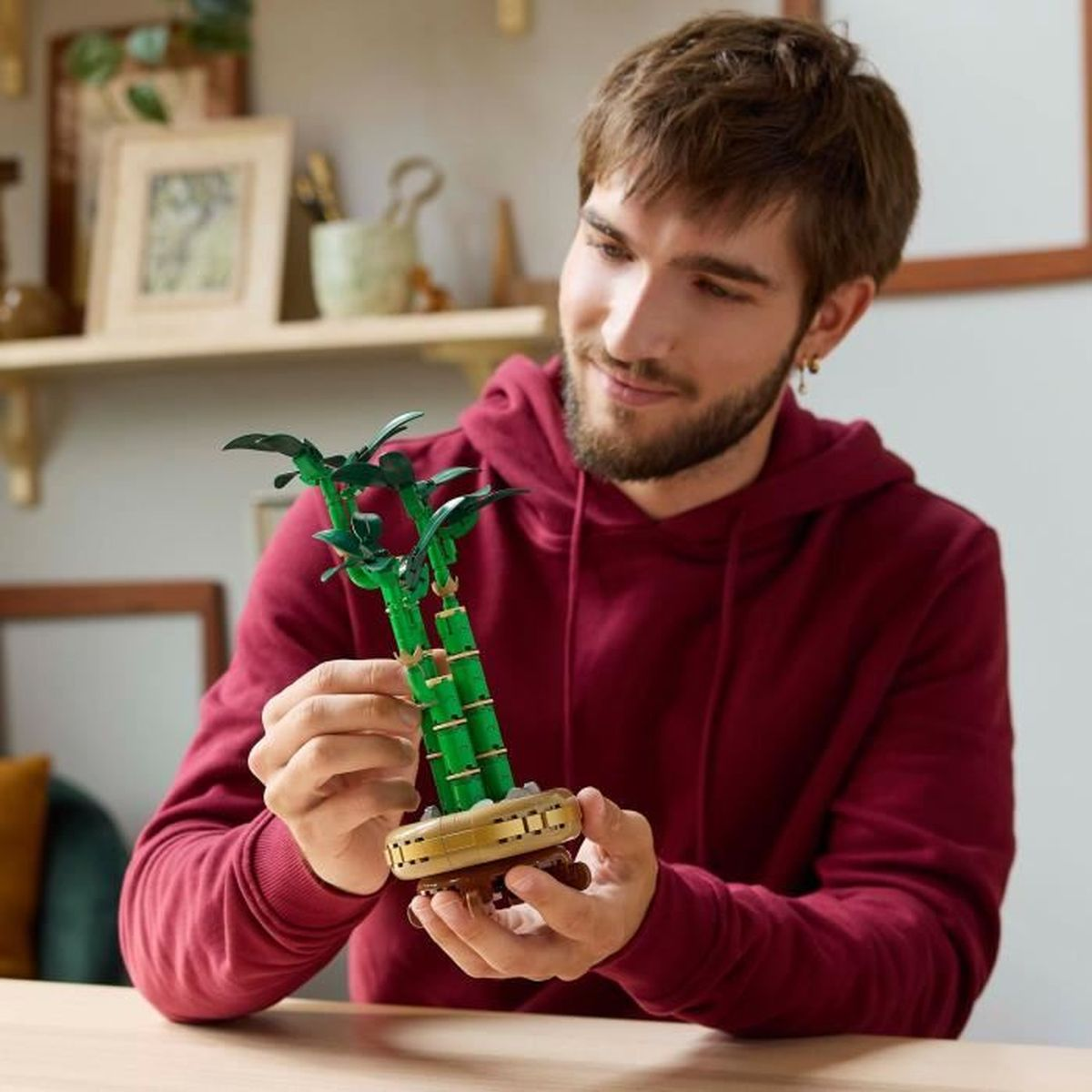 Een man houdt een Lego bonsai-boom vast. De boom is groen en bruin, en de man glimlacht.