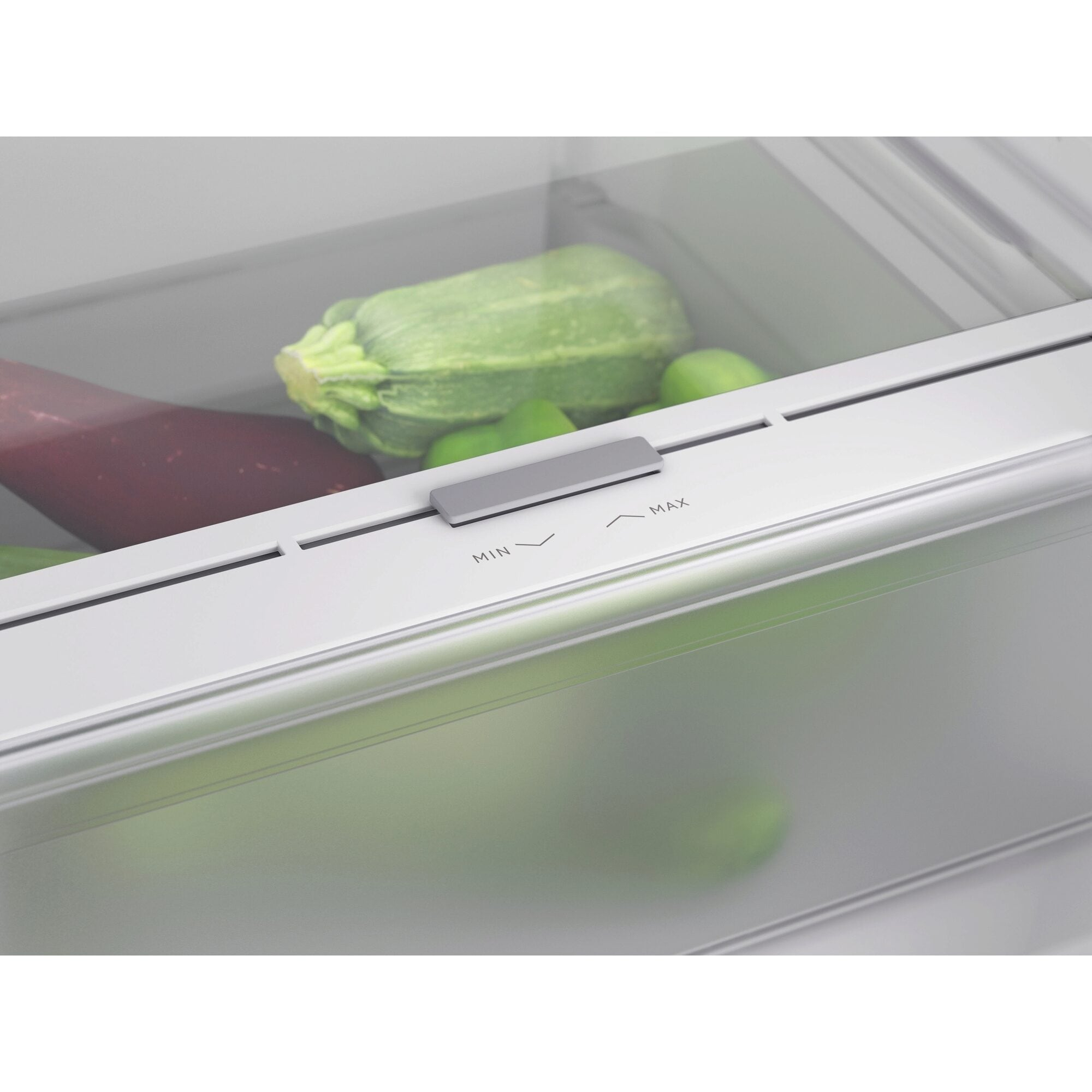Dentro de un cajón de refrigerador con verduras. Calabacín verde, verdura roja y limas verdes, interior blanco.