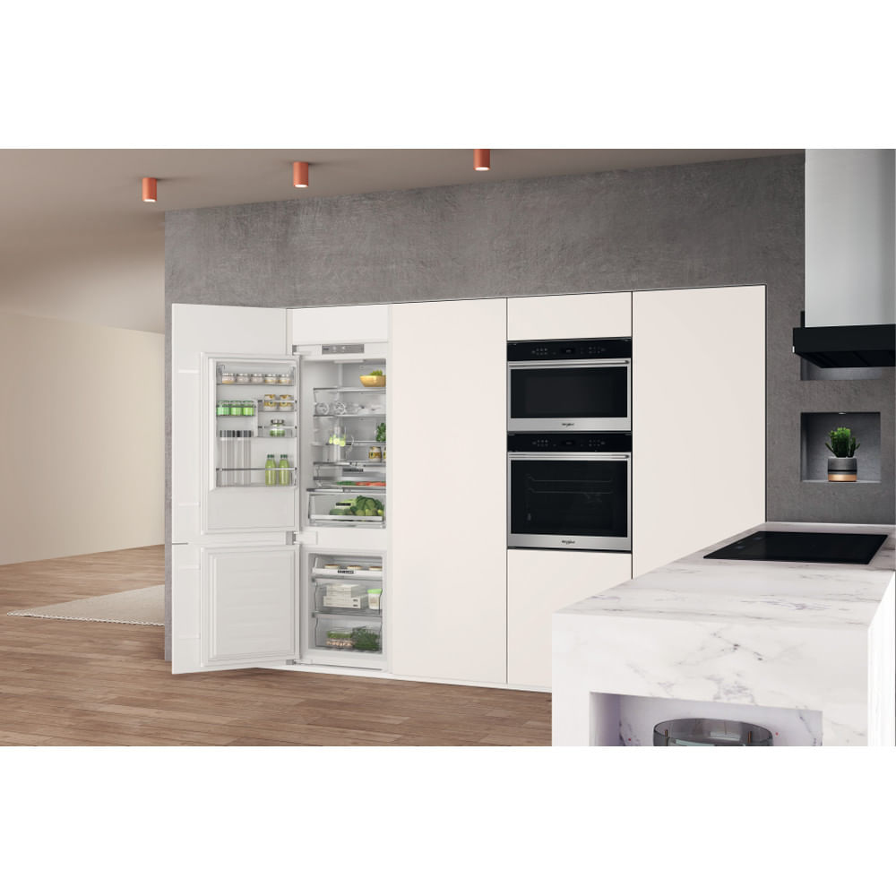 Una cucina con frigorifero e forni a incasso. La porta del frigorifero è aperta.