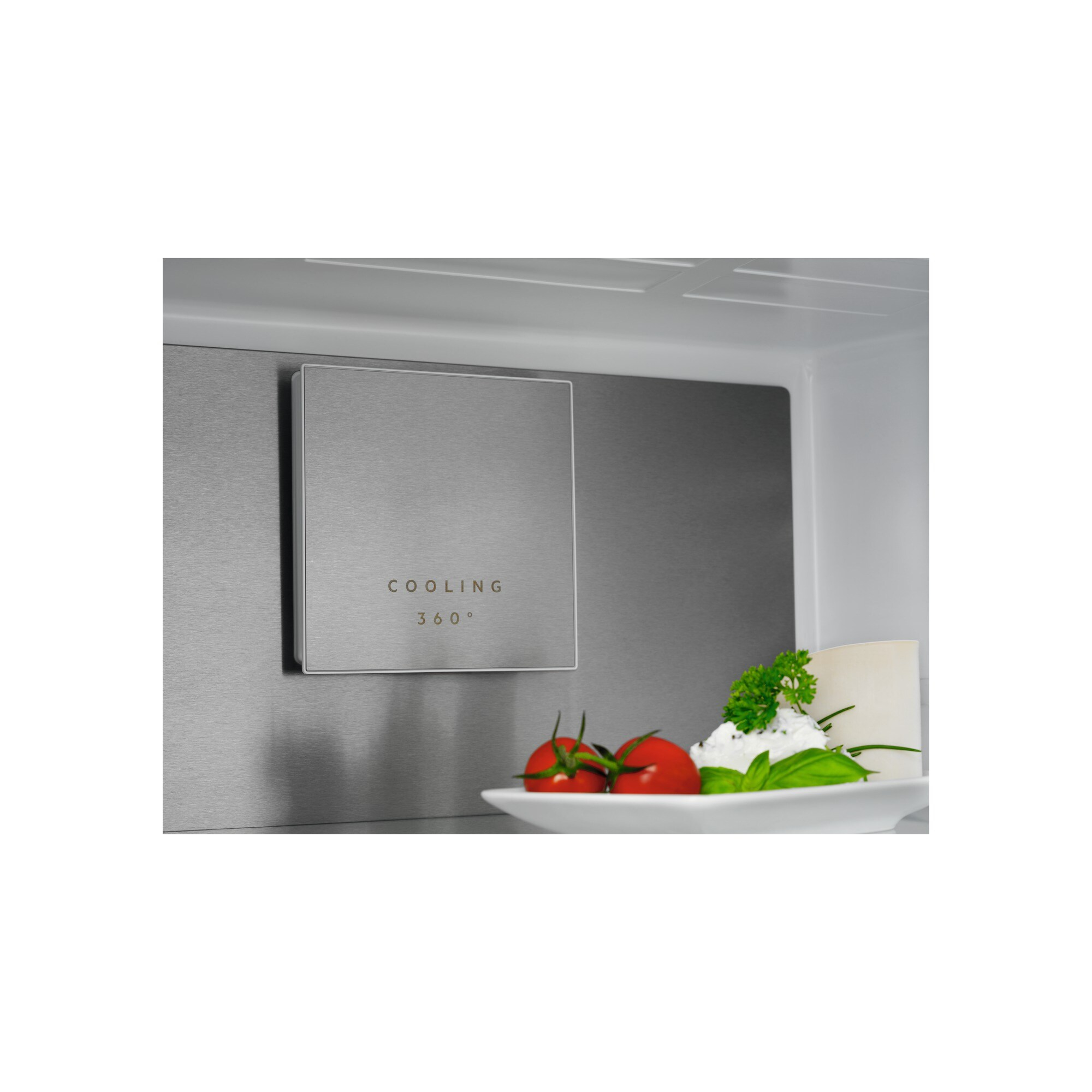 Primer plano del interior de un refrigerador. Muestra una unidad de enfriamiento y un plato con tomates y albahaca.
