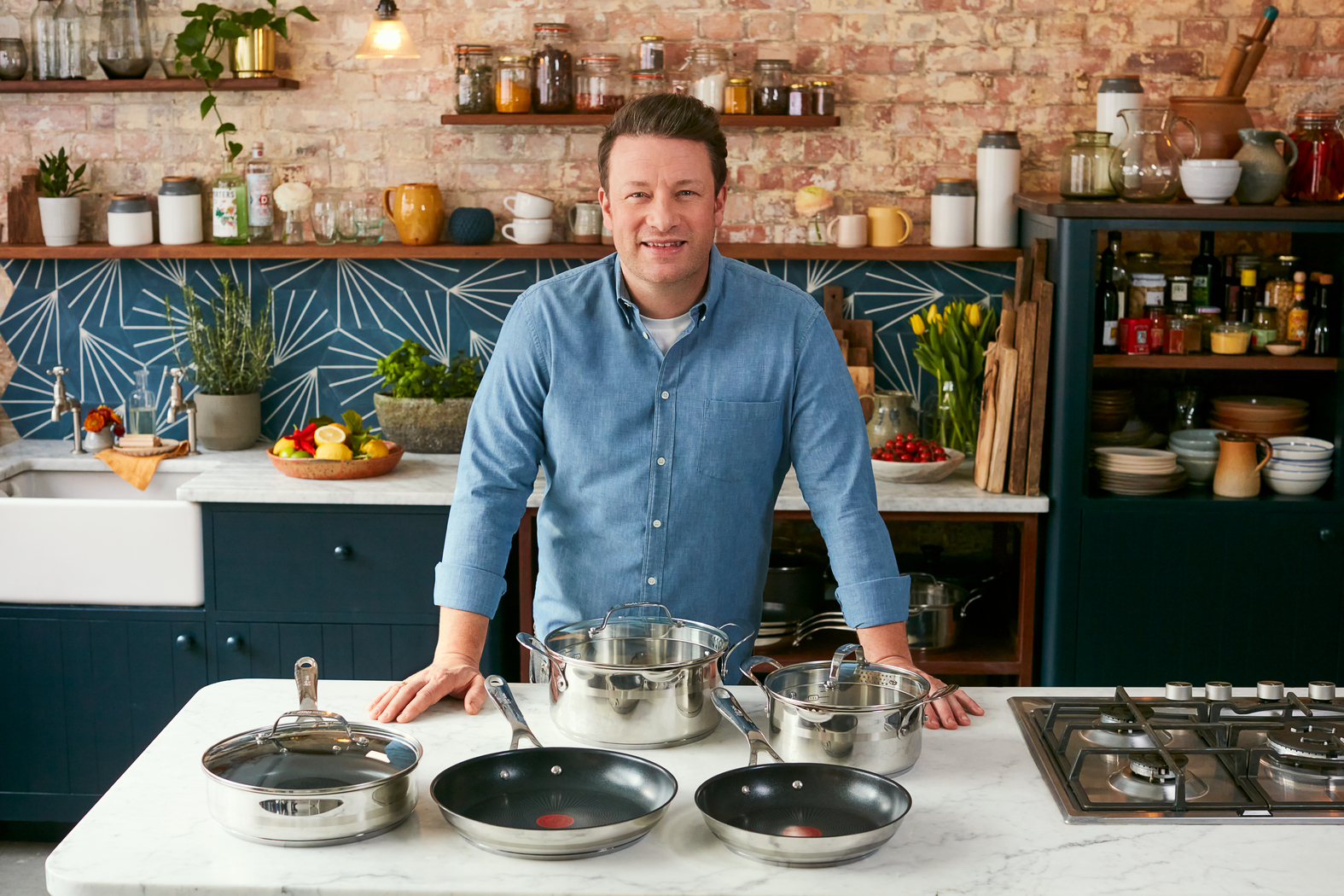 Jamie Oliver avec des casseroles et des poêles de cuisine. Il se tient devant la cuisinière.
