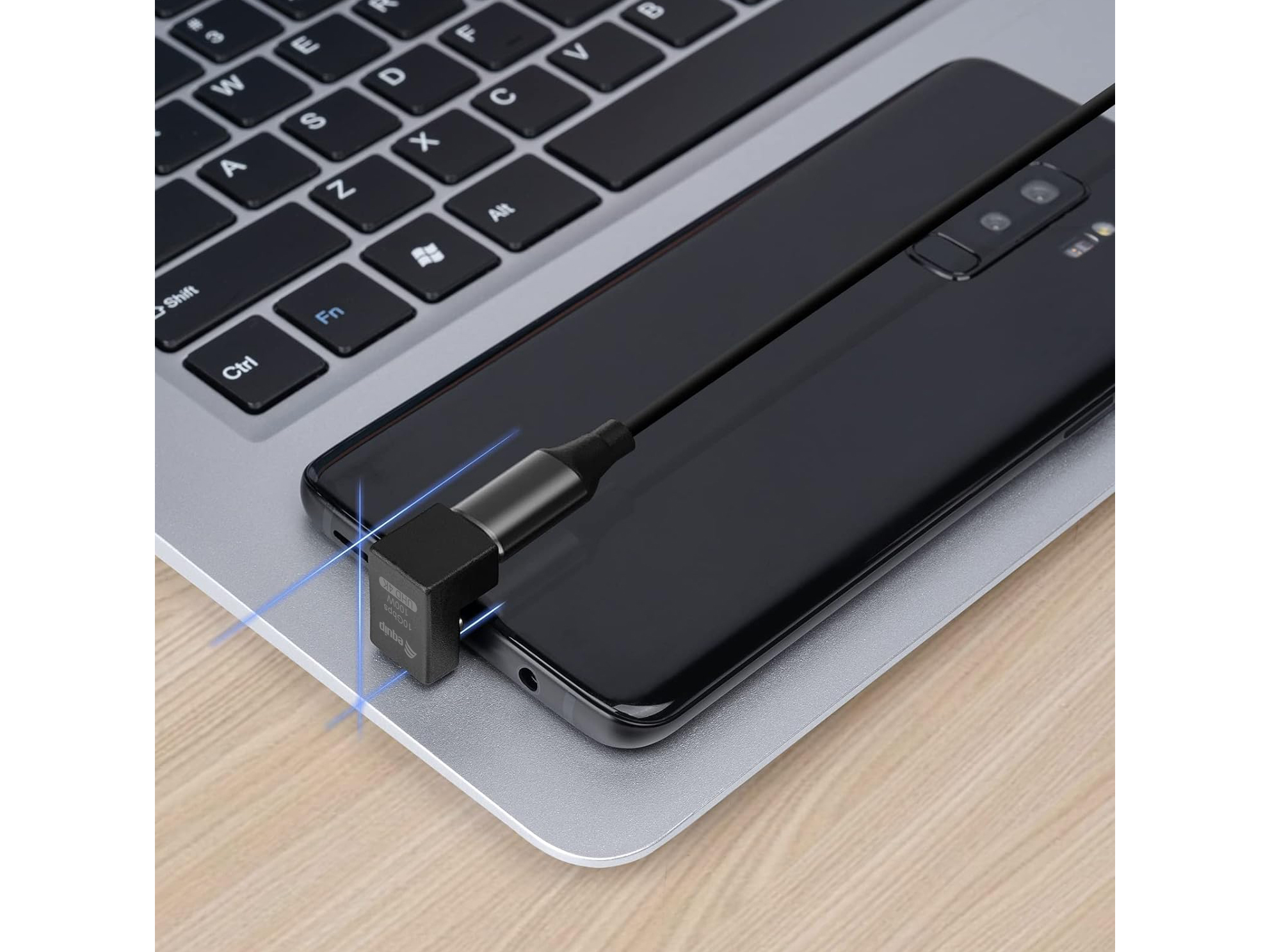 Teléfono conectado a una laptop con un cable negro y un adaptador USB-C. El teléfono es negro.