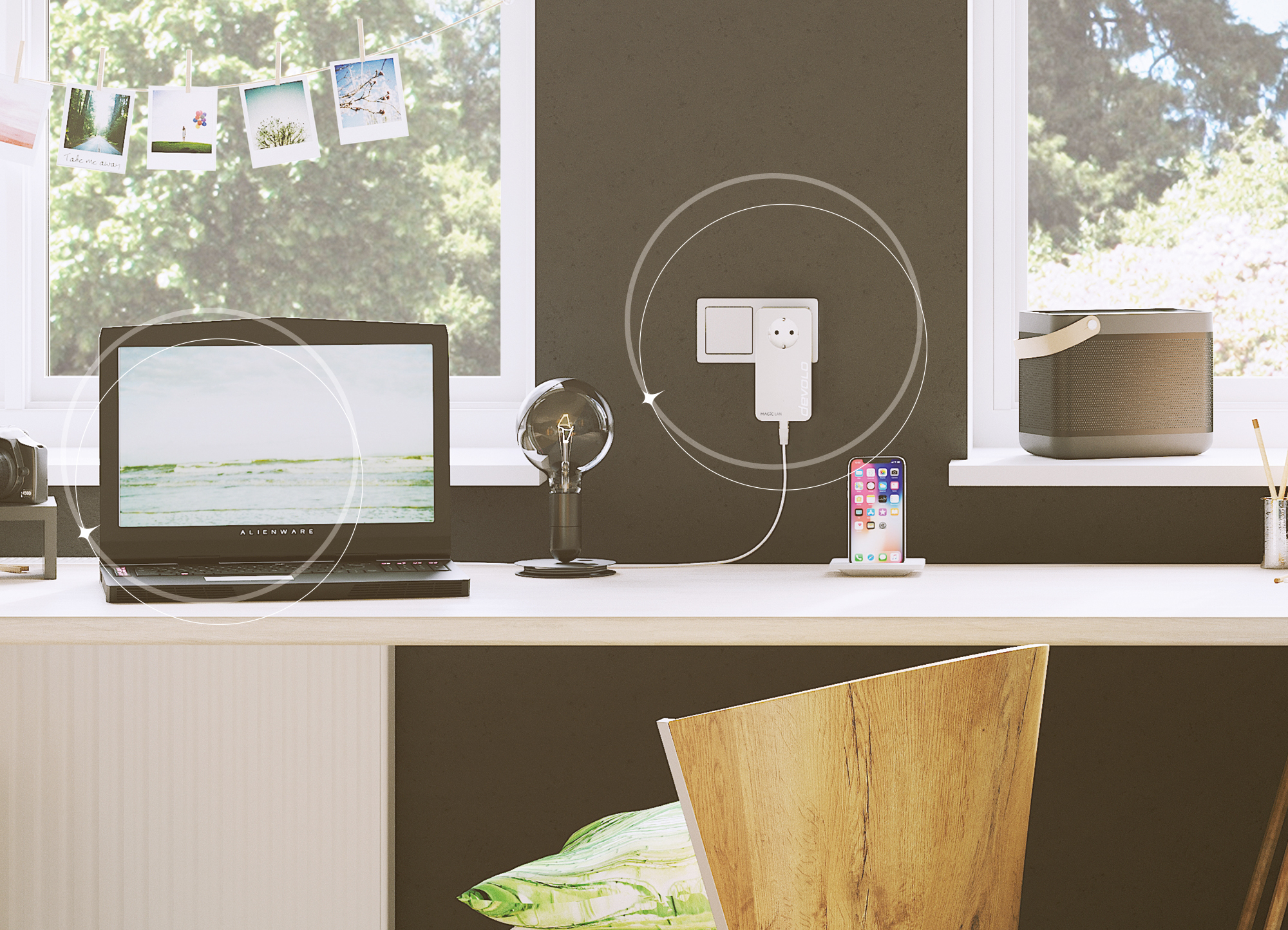 Laptop, lampa, ładowanie telefonu. Drewniane krzesło. Białe biurko, okna i zielone liście w tle.