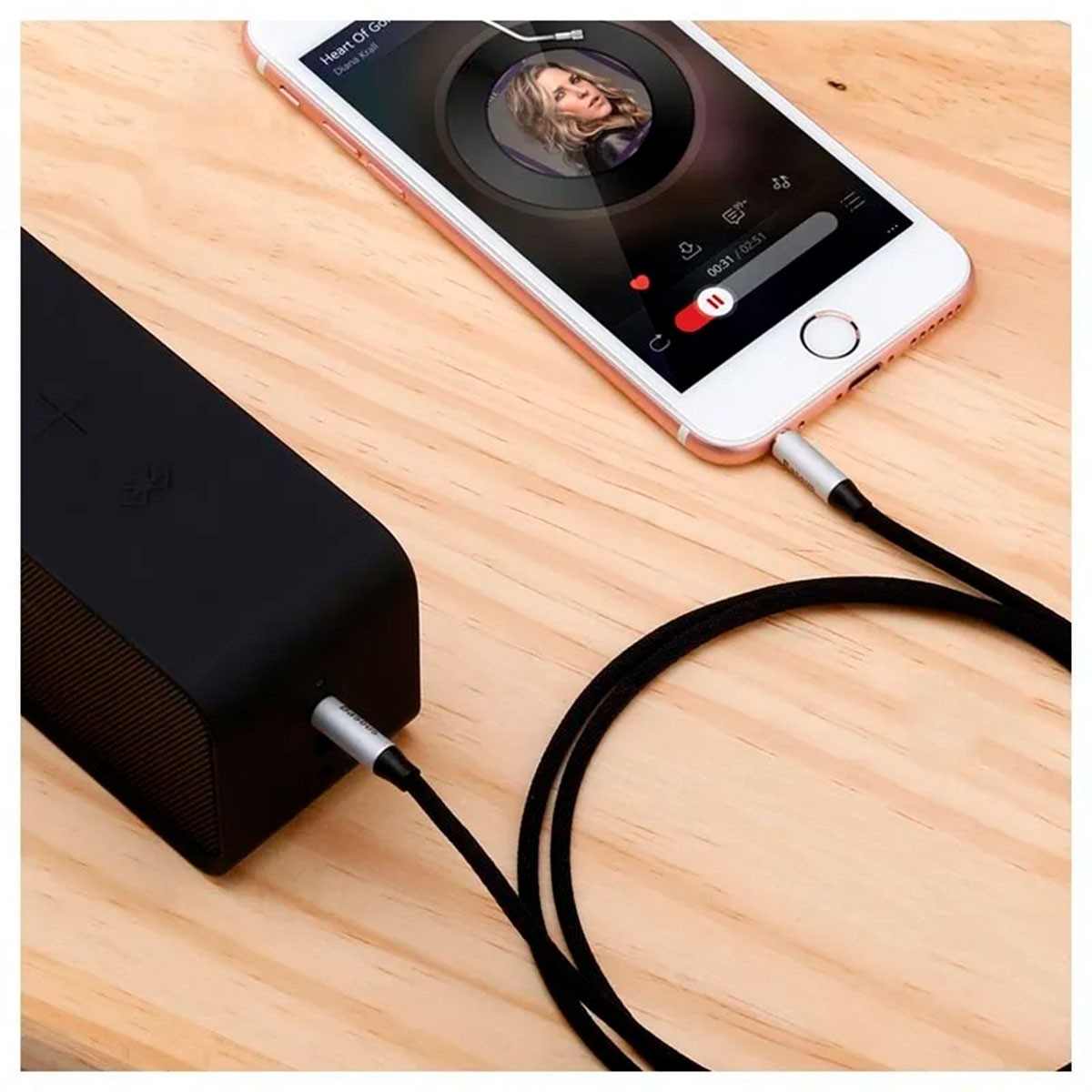 Telefon i głośnik połączone kablem audio. Drewniana powierzchnia.