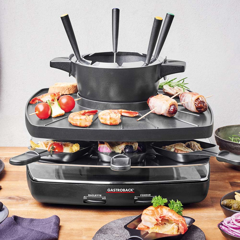Ein schwarzer Fonduegrill mit Speisen obenauf, bereit zum Kochen. Holztisch.