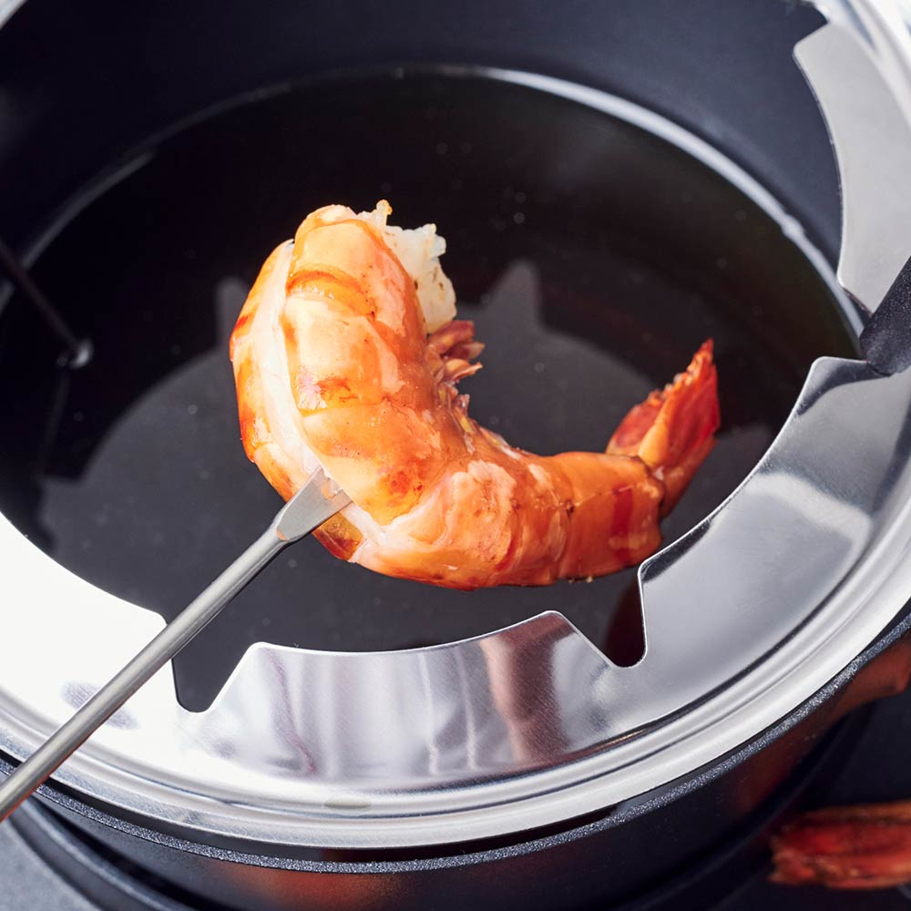Garnelen, die in einem Fonduetopf mit heißem Öl gekocht werden. Eine Gabel hält die Garnele über dem Öl.