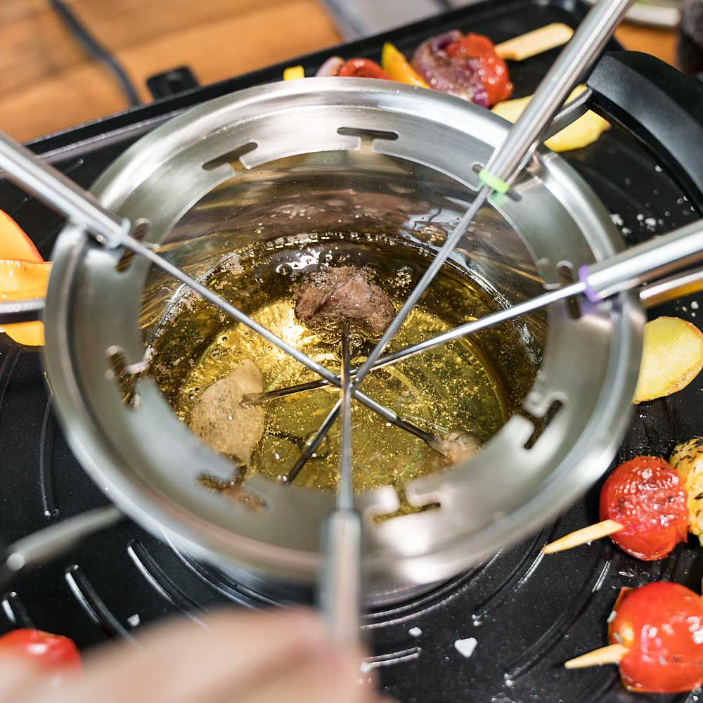 Una pentola per fonduta con cibo che cuoce all'interno, con spiedini attorno alla pentola.
