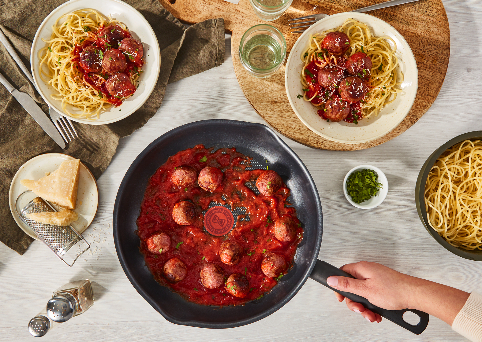 Widok z góry na spaghetti z klopsikami, patelnią i składnikami na stole.