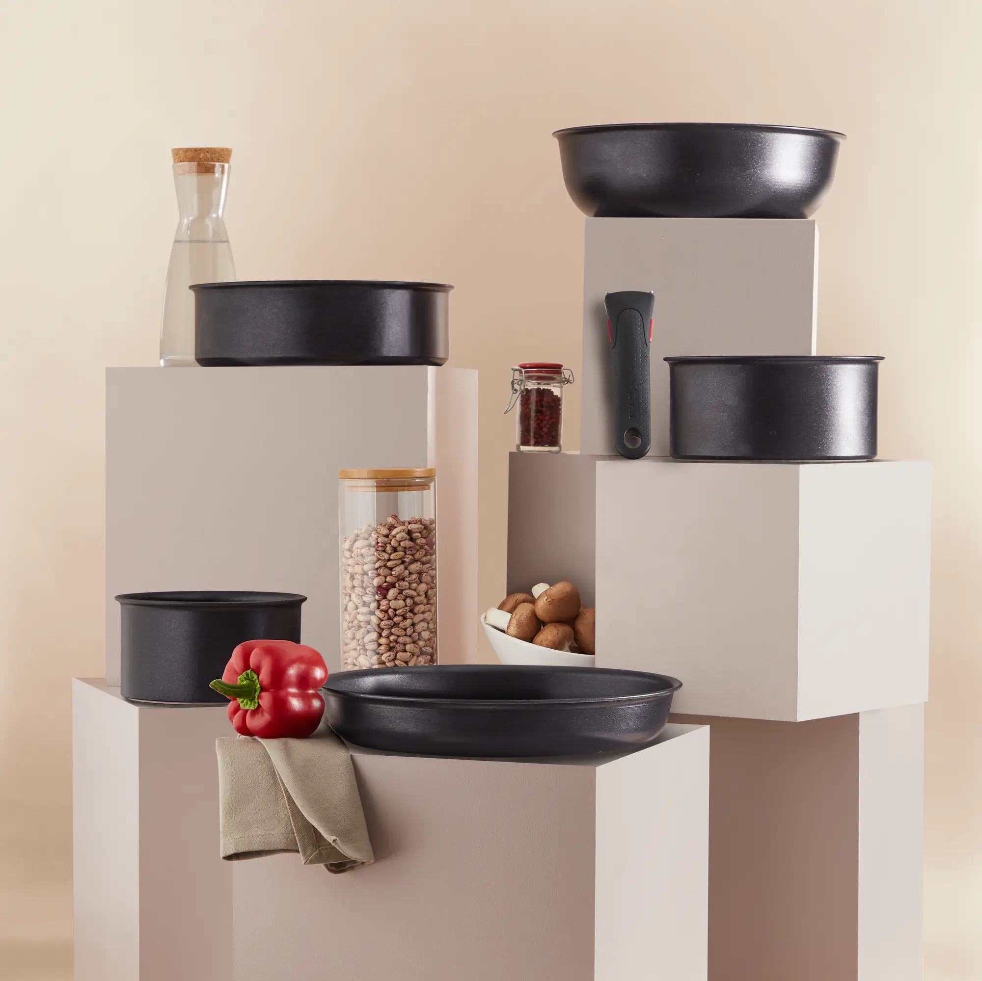 Różne czarne garnki i słoiki na białych postumentach, z jedzeniem i szklaną butelką.