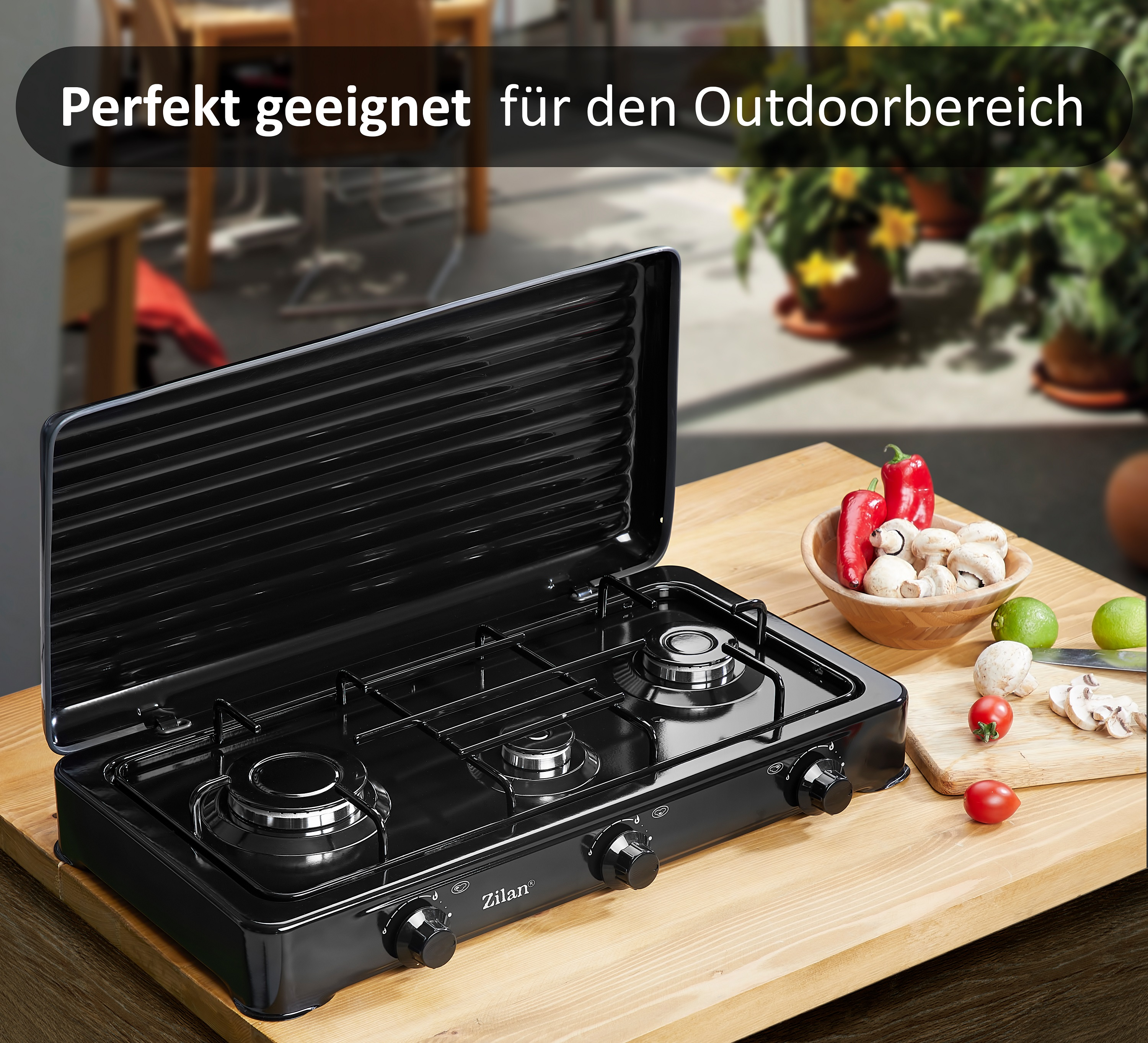 Czarna kuchenka z trzema palnikami i drewniana deska do krojenia z warzywami.