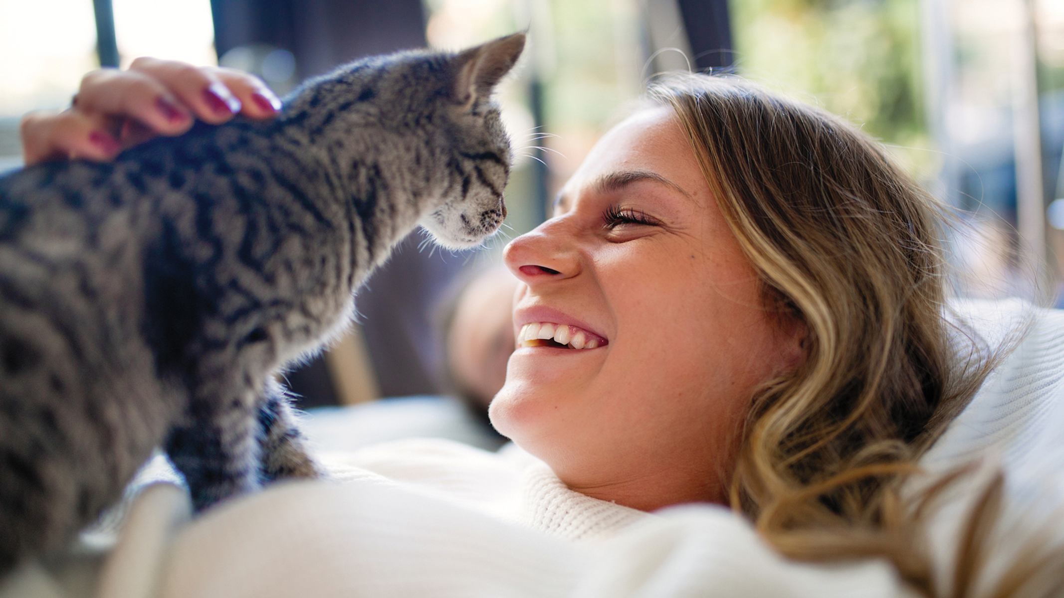 Vrouw met kat. Ze lacht en aait de kat. Zonnestralen aanwezig.