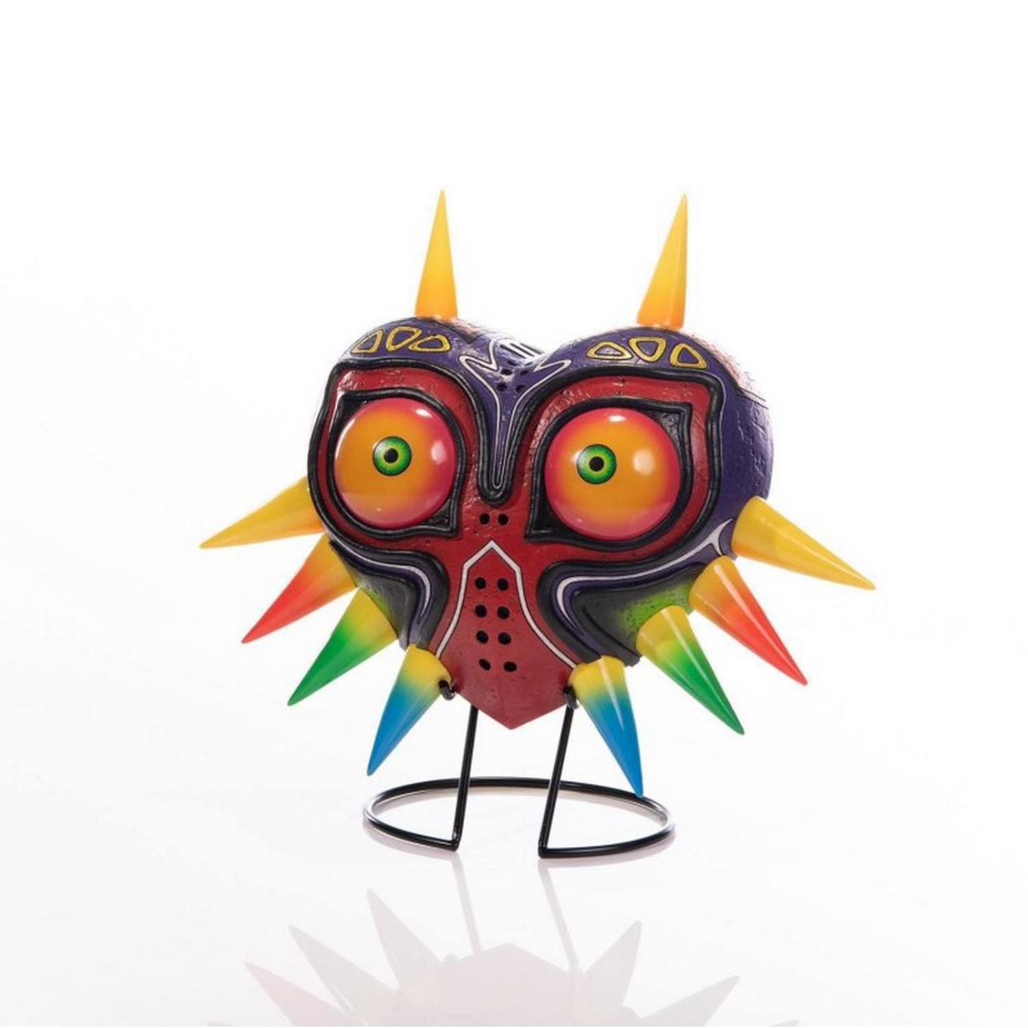 Eine Nachbildung der Majora's Mask auf einem Ständer. Die Maske ist rot, gelb und lila. Weißer Hintergrund.