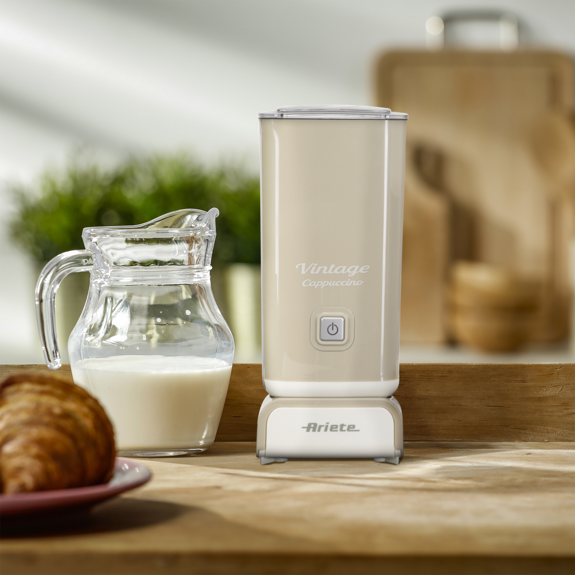 Ein cremefarbener Milchaufschäumer und eine Glaskanne mit Milch und einem Croissant.